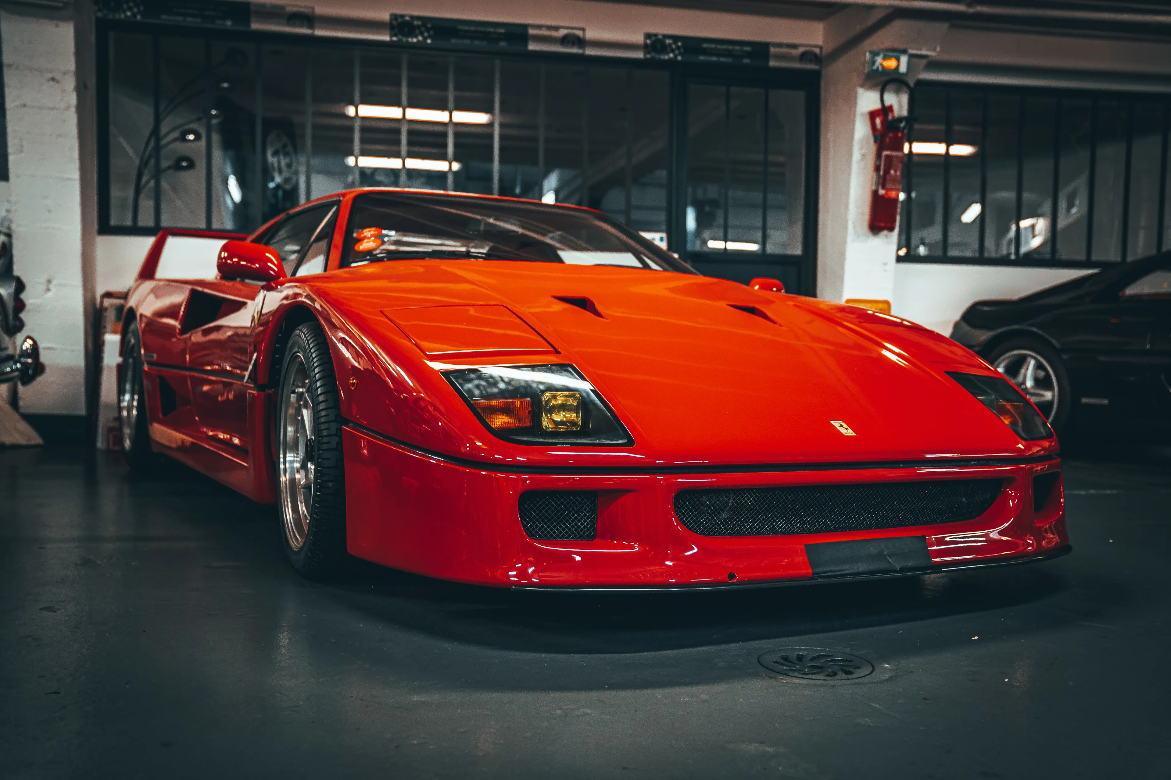 A vibrant red Ferrari, a classic type of car, parked indoors with other vehicles faintly visible in the background.