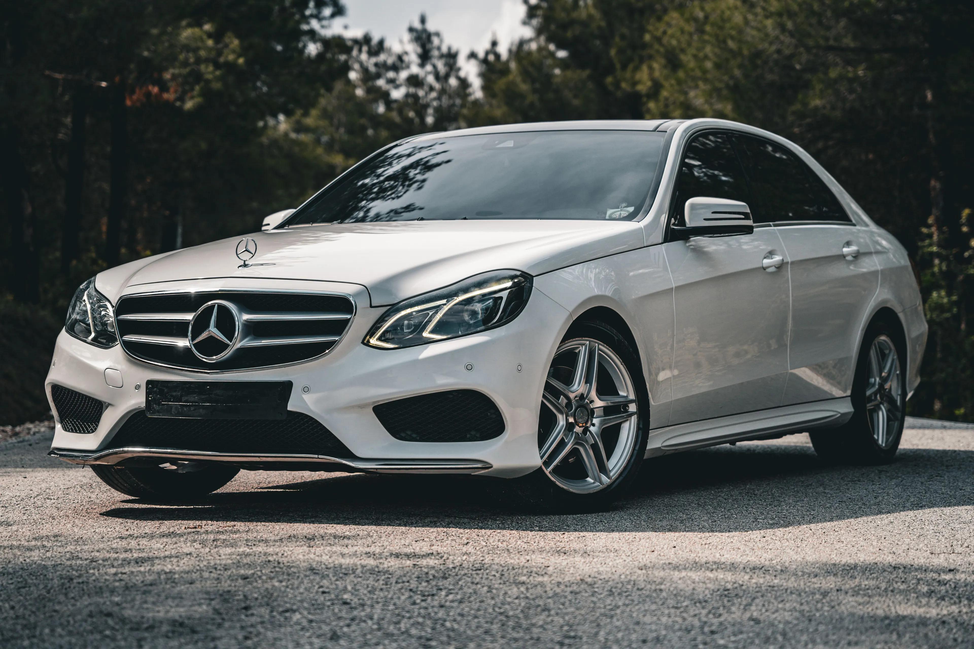 A white Mercedes car parked on an asphalt road with trees in the background. A type of car with a sleek design.