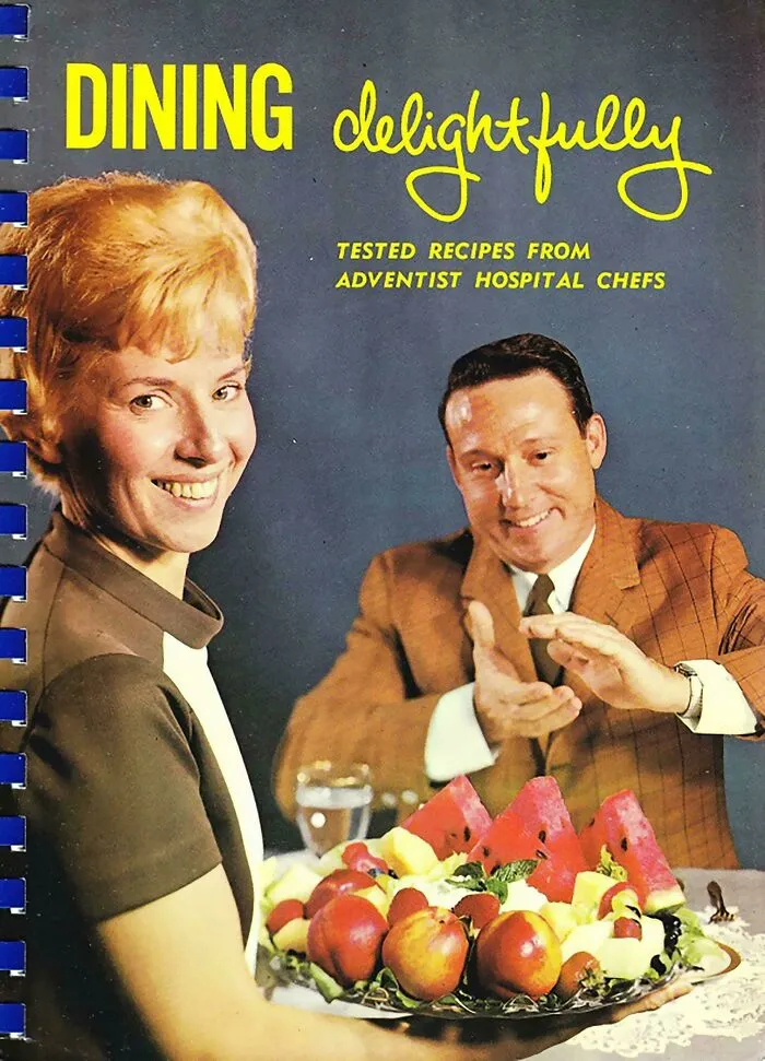 Vintage cookbook cover featuring a smiling couple and a platter of fruit in a hilariously unhinged style