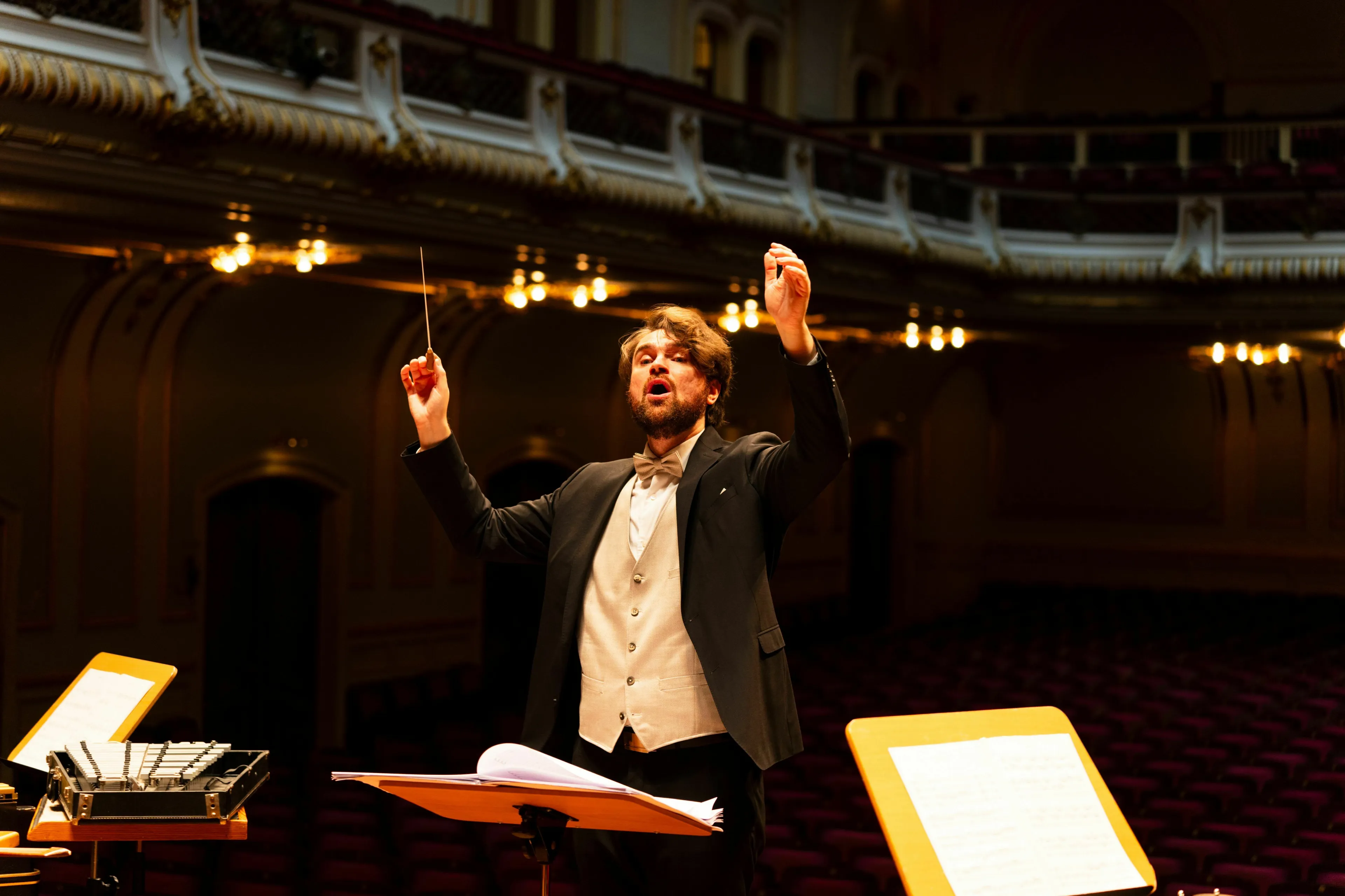 A conductor in a classical music hall, intensely leading an orchestra with raised hands and a baton. Test your General Knowledge.