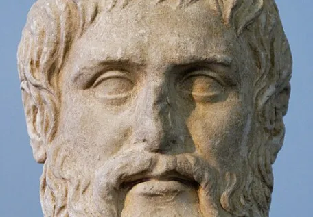 A close-up of a weathered stone bust of the philosopher Plato, featuring a beard and defined facial features.