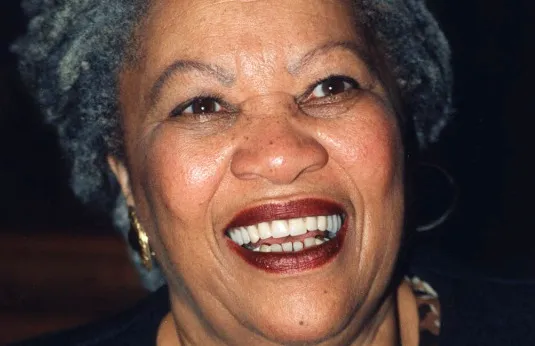 Toni Morrison, smiling brightly with grey hair and gold earrings, Nobel Prize in Literature winner, featured close-up.
