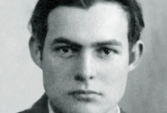 A black and white close-up photo of author Ernest Hemingway, looking directly at the camera. Nobel Prize in Literature.