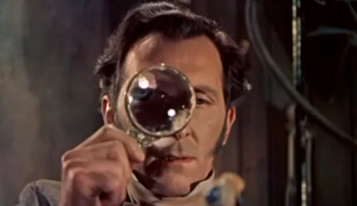 A man with sideburns and dark hair looking through a large magnifying glass. How well-read are you? Dr. Frankenstein.