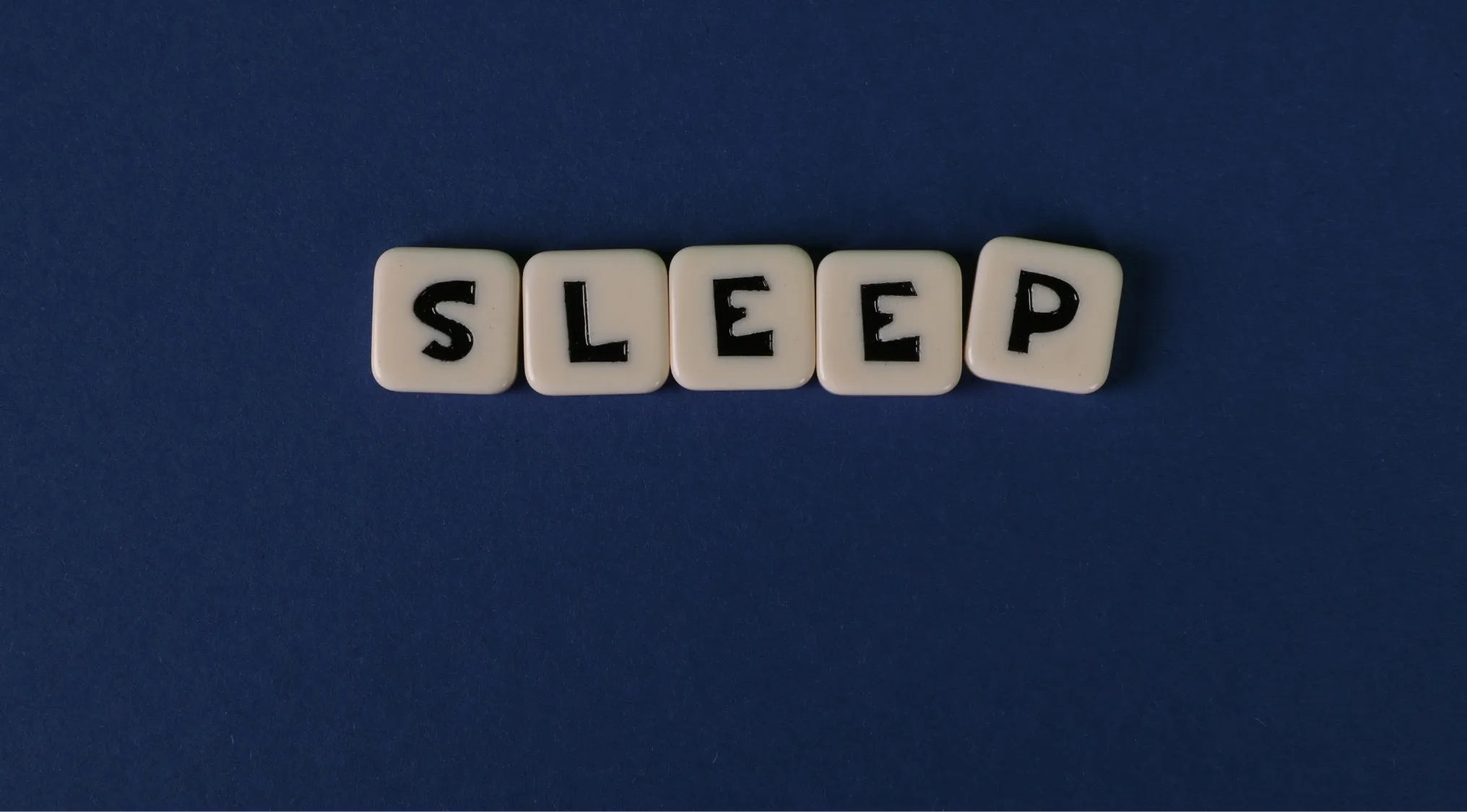 The word "SLEEP" spelled out in scrabble tiles on a dark blue background. Explores the hormone regulating the sleep-wake cycle.