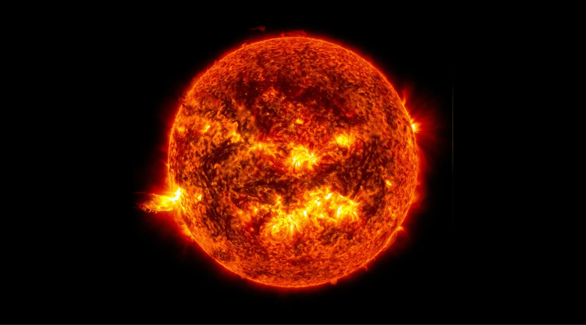 A fiery red and orange image of the Sun, with bright flares and activity across its visible layer. Science Quiz.