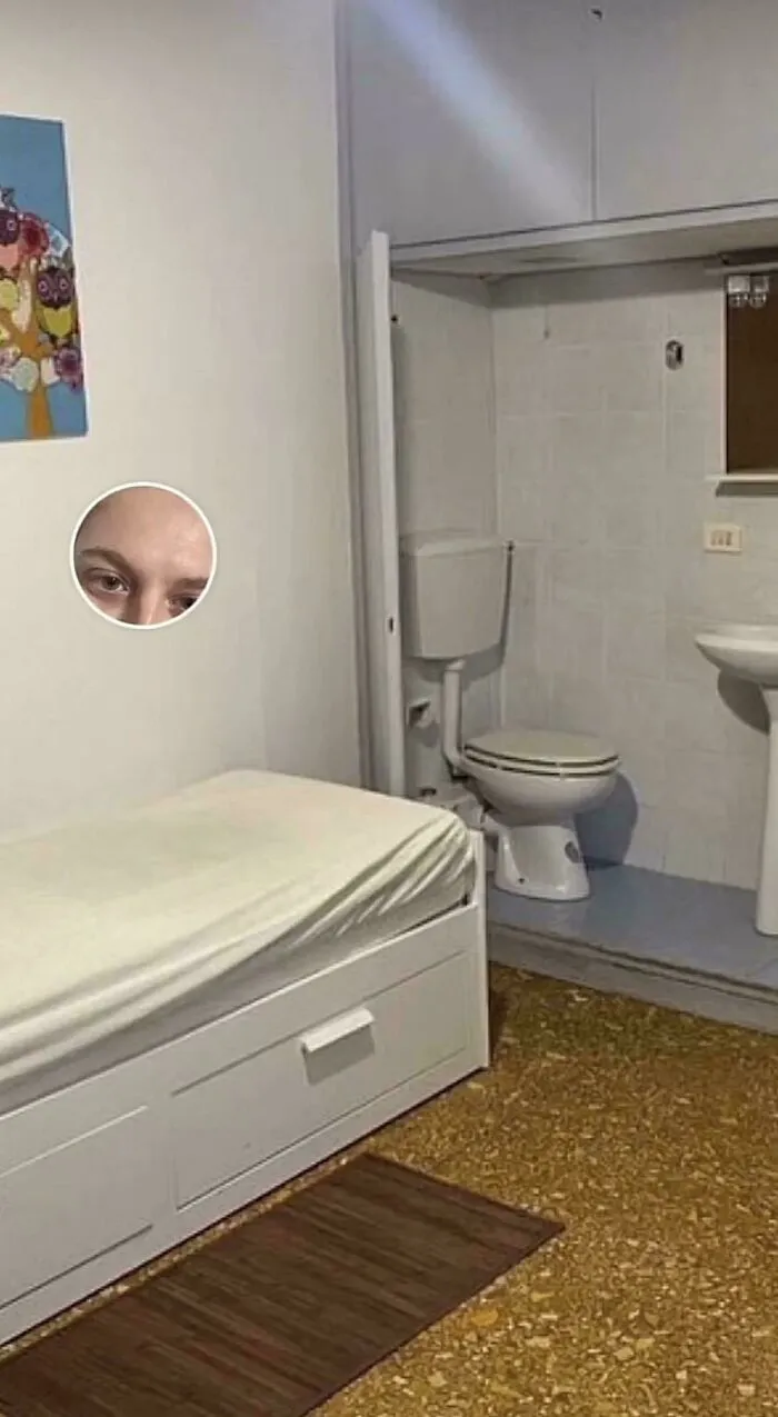 A small bedroom with a bed directly adjacent to a toilet and sink, from unhinged real estate listings.