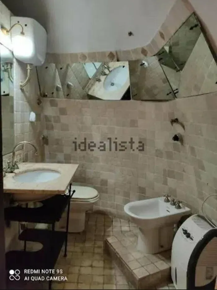 A peculiar real estate listing showing a bathroom with irregularly shaped, mismatched mirrors and beige tiles.