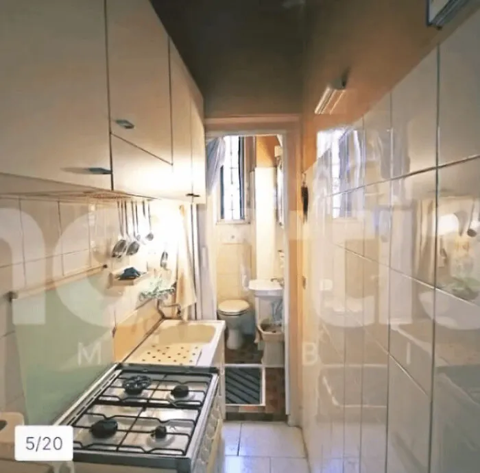 A narrow, unhinged real estate listing kitchen with a stove and sink, leading to a small bathroom.