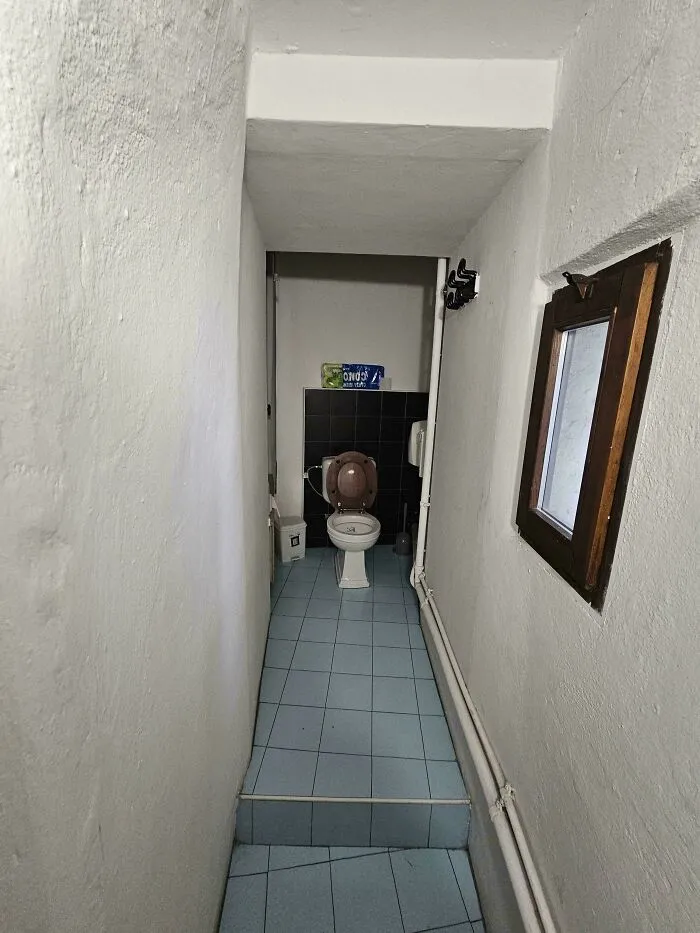 A narrow, unappealing hallway leading to a small, isolated toilet, representing unhinged real estate listings.