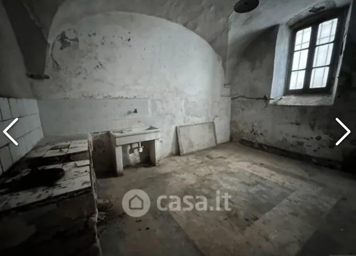 A very run-down and unhinged real estate listing, featuring a dilapidated room with a single sink and dirty walls.