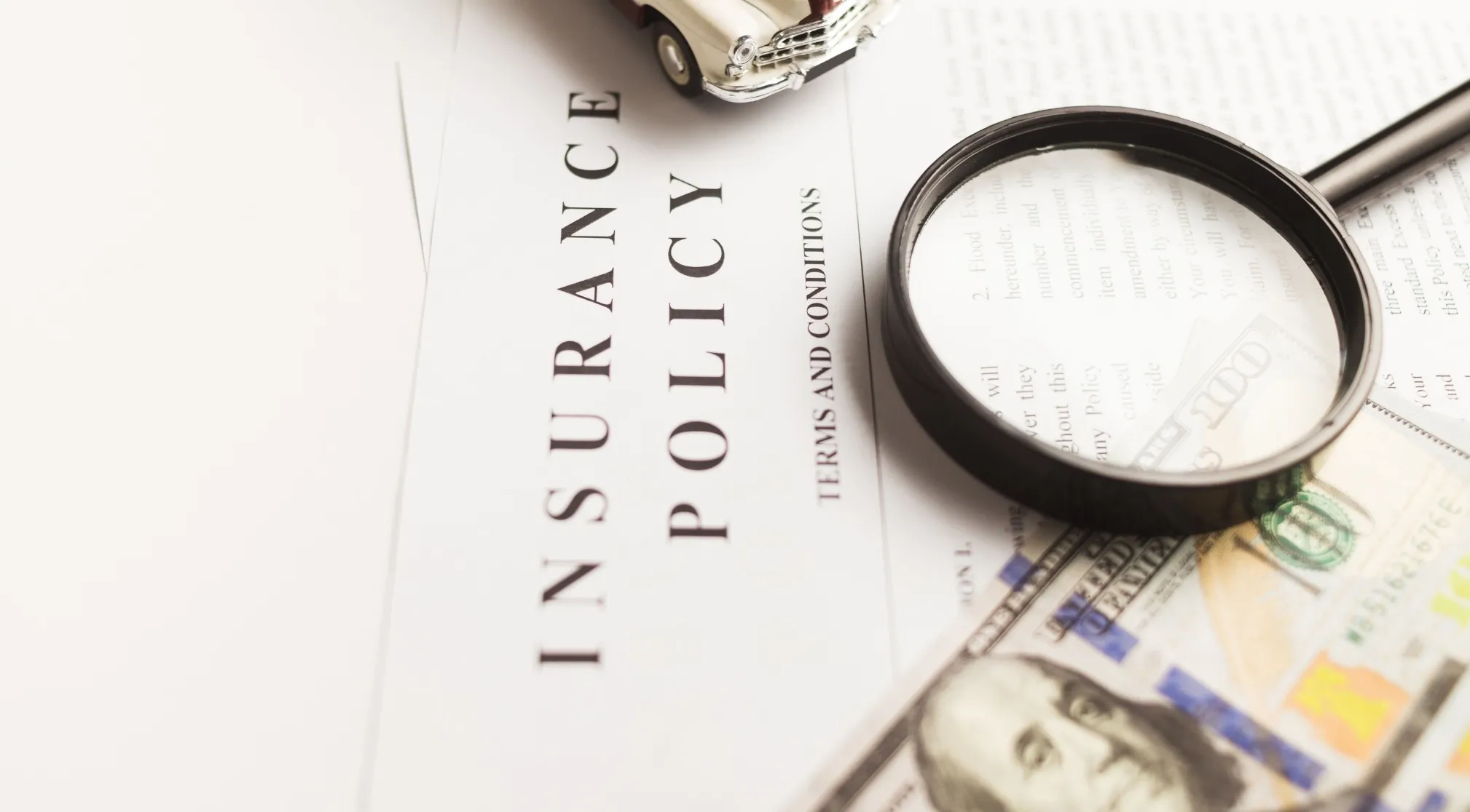 A magnifying glass on an insurance policy document with a toy car and money, explaining deductible.