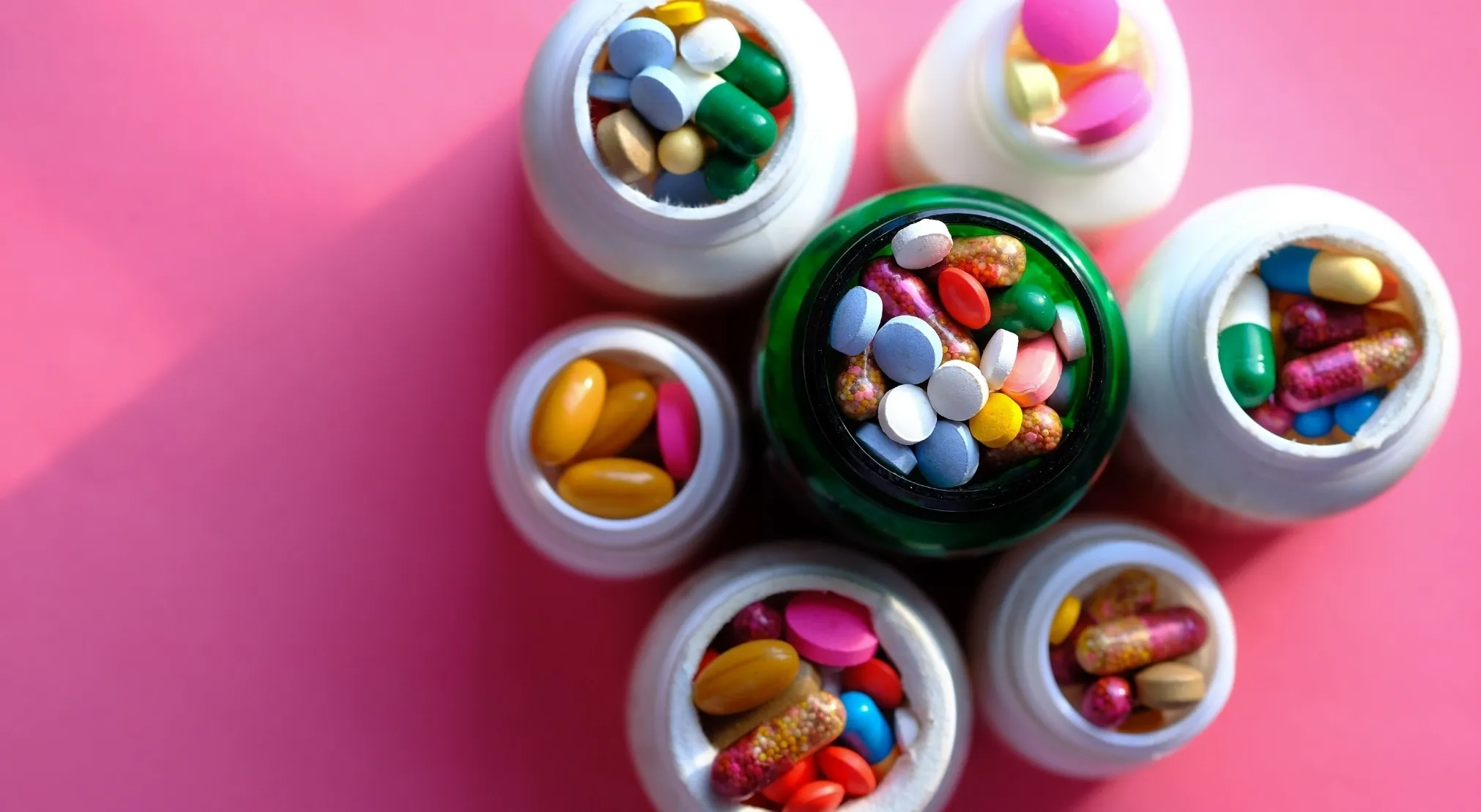 Variety of colorful medications in bottles on a pink background, highlighting safe disposal of unused medications.
