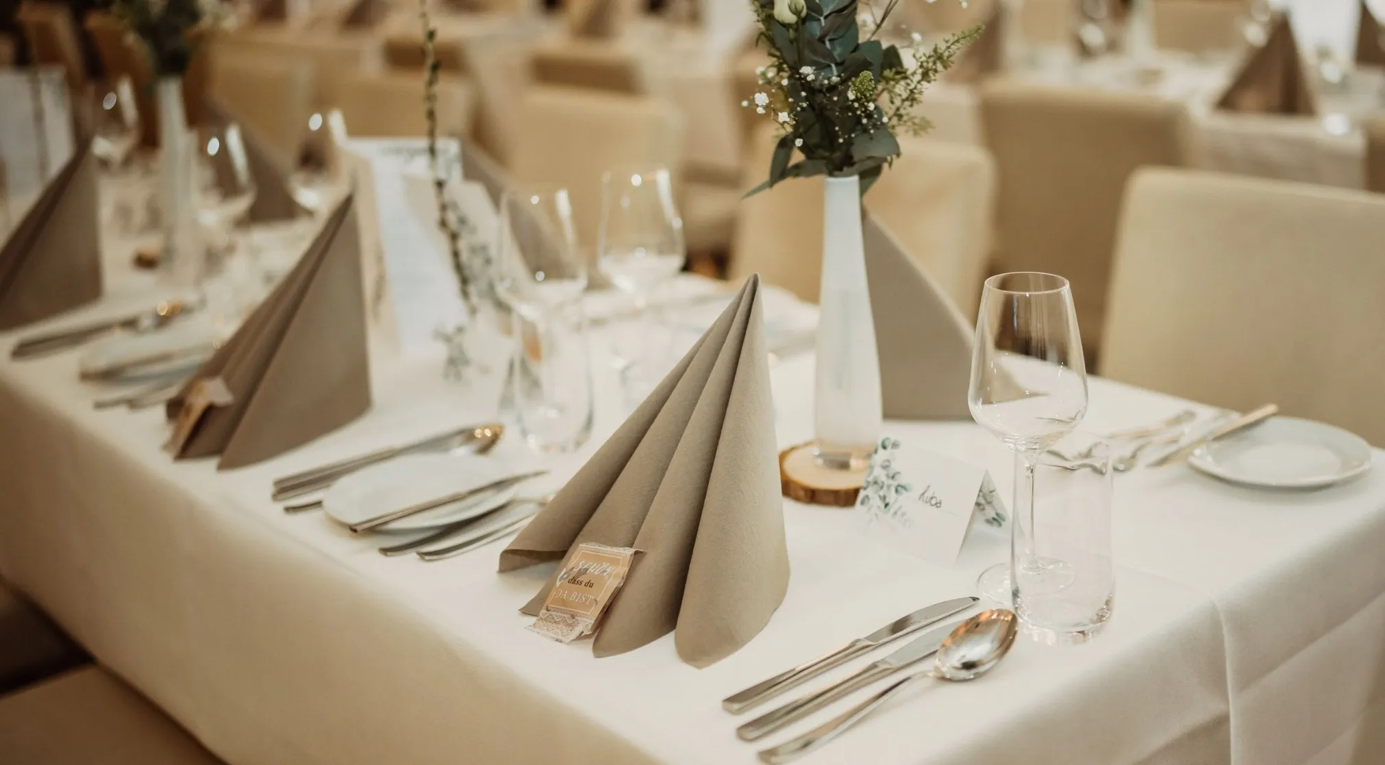 A well-set dining table with beige napkins and cutlery. Learn proper napkin etiquette with this Adulting Quiz.