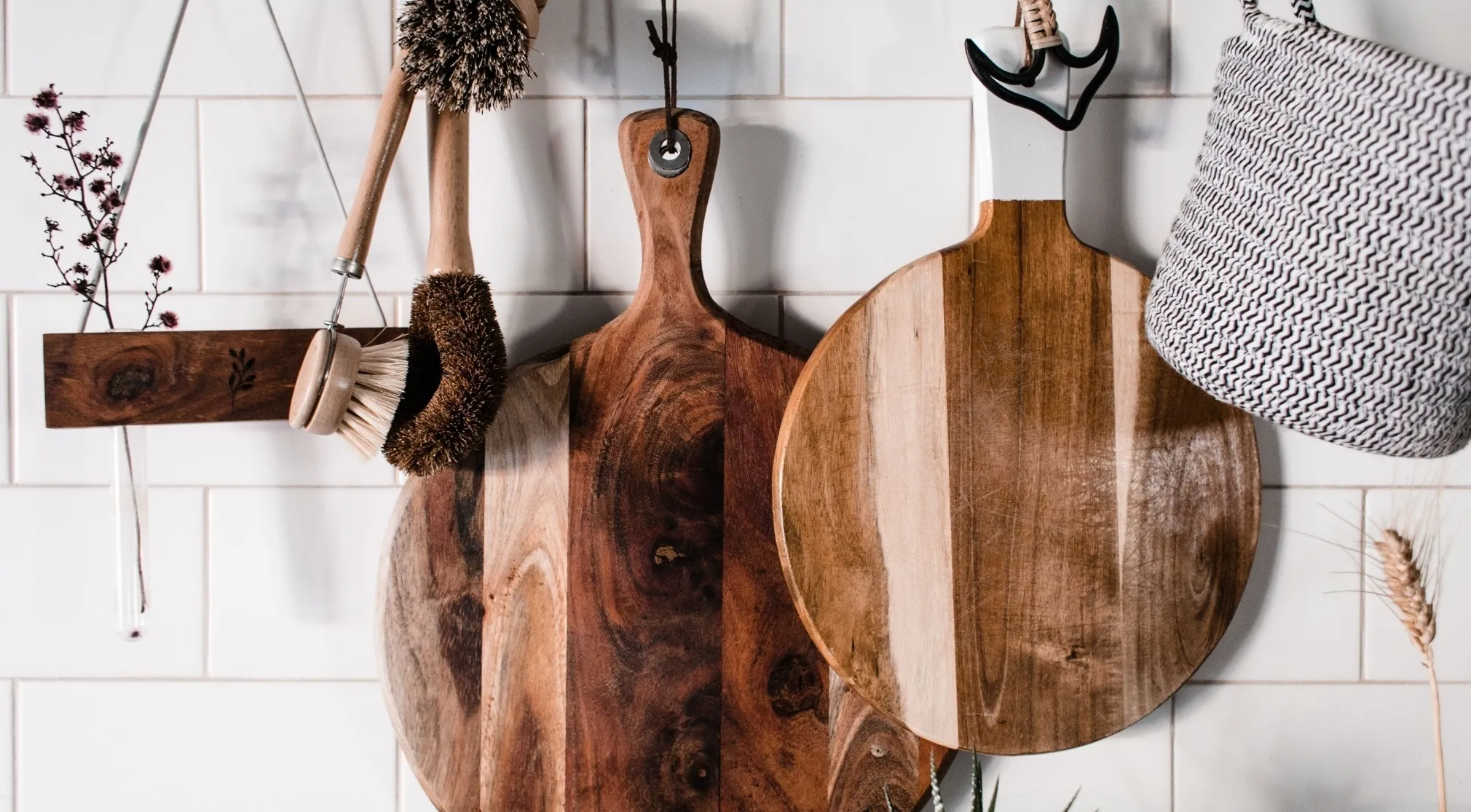 Wooden cutting boards hang on a white tiled wall with kitchen brushes. Reduce food contamination.