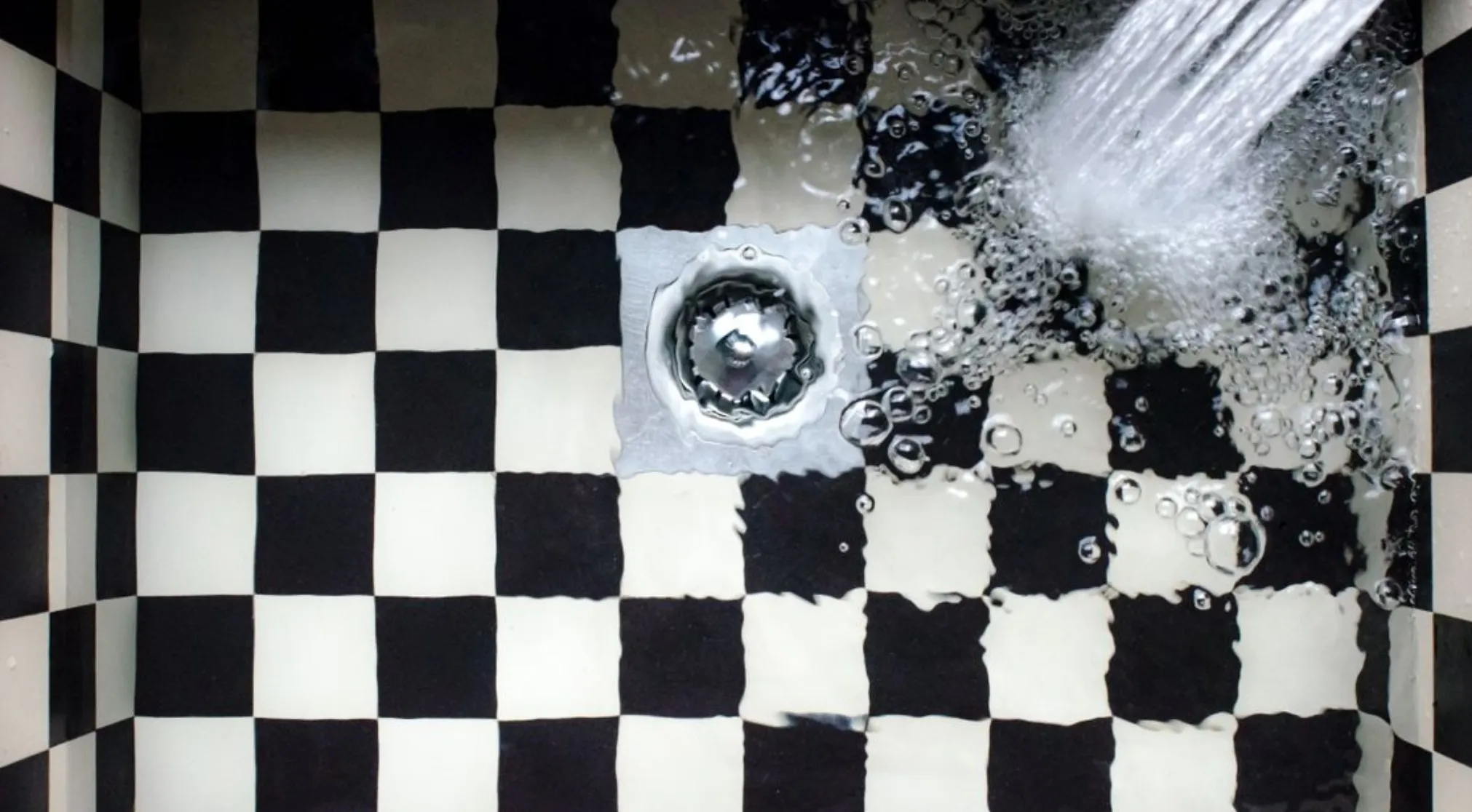 Water flowing into a black and white checkered sink, with the drain at the bottom. The main SEO keyword is clogged kitchen sink drain.