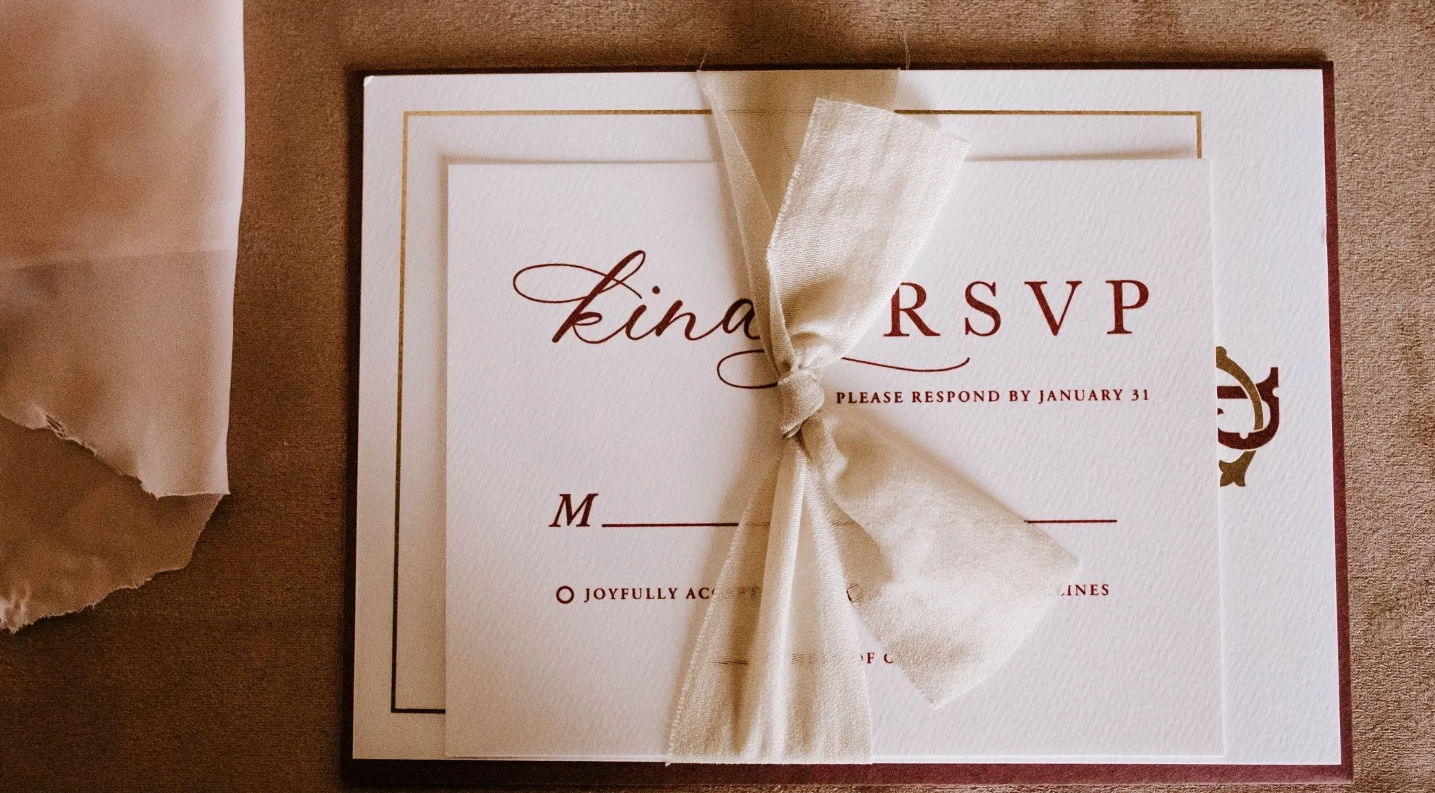 An elegant wedding invitation with RSVP, tied with a cream ribbon, asking guests to respond by January 31.