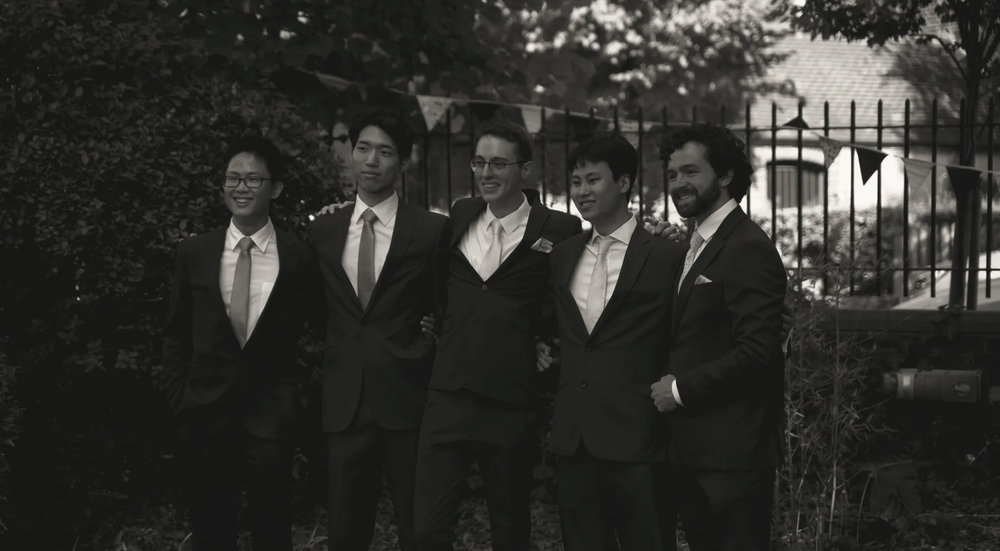 Five men in black suits and light ties, some smiling, standing together. What does a white tie dress code mean for men?