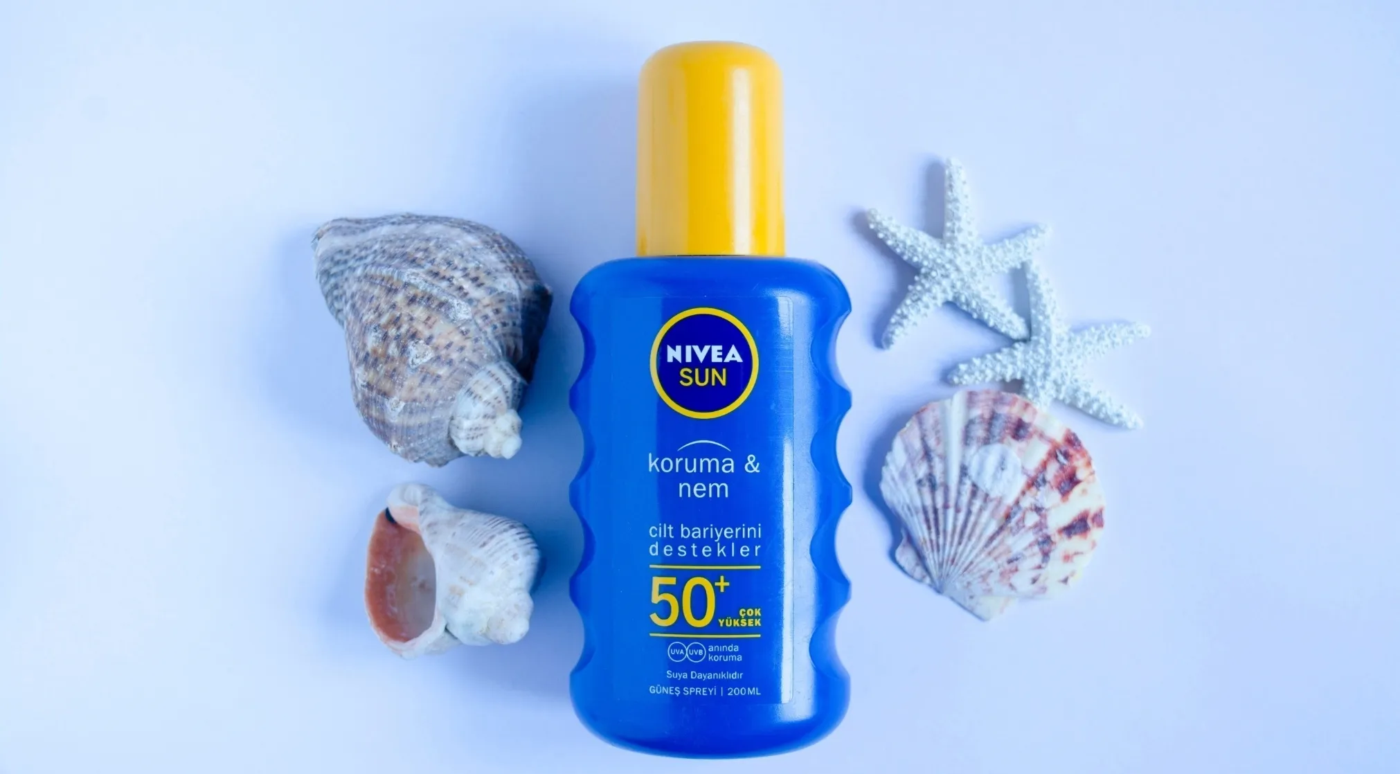 A Nivea Sun sunscreen bottle with seashells and starfish on a white background, suggesting extended outdoor activity and sun protection.