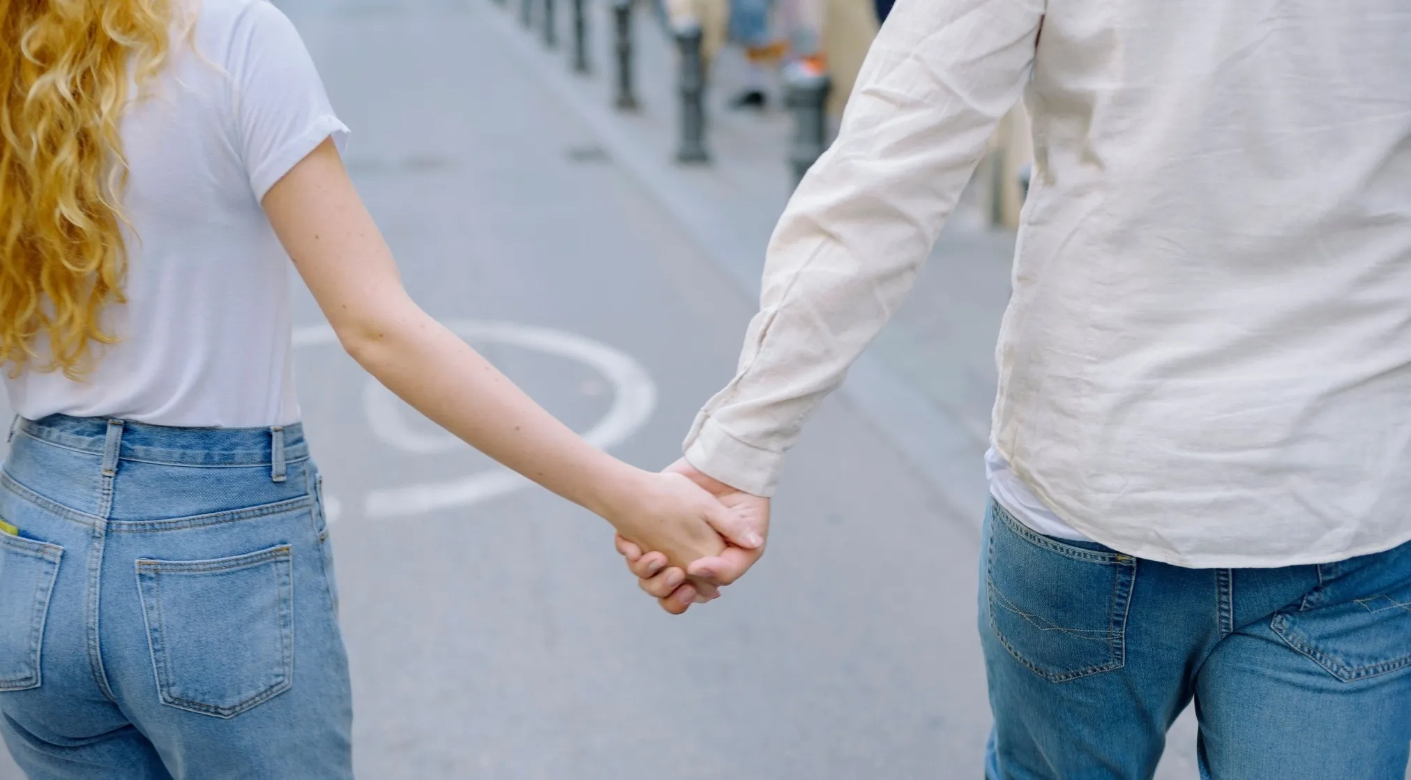 A couple holding hands while walking on a sidewalk. The gentleman is to the right, lady to the left.