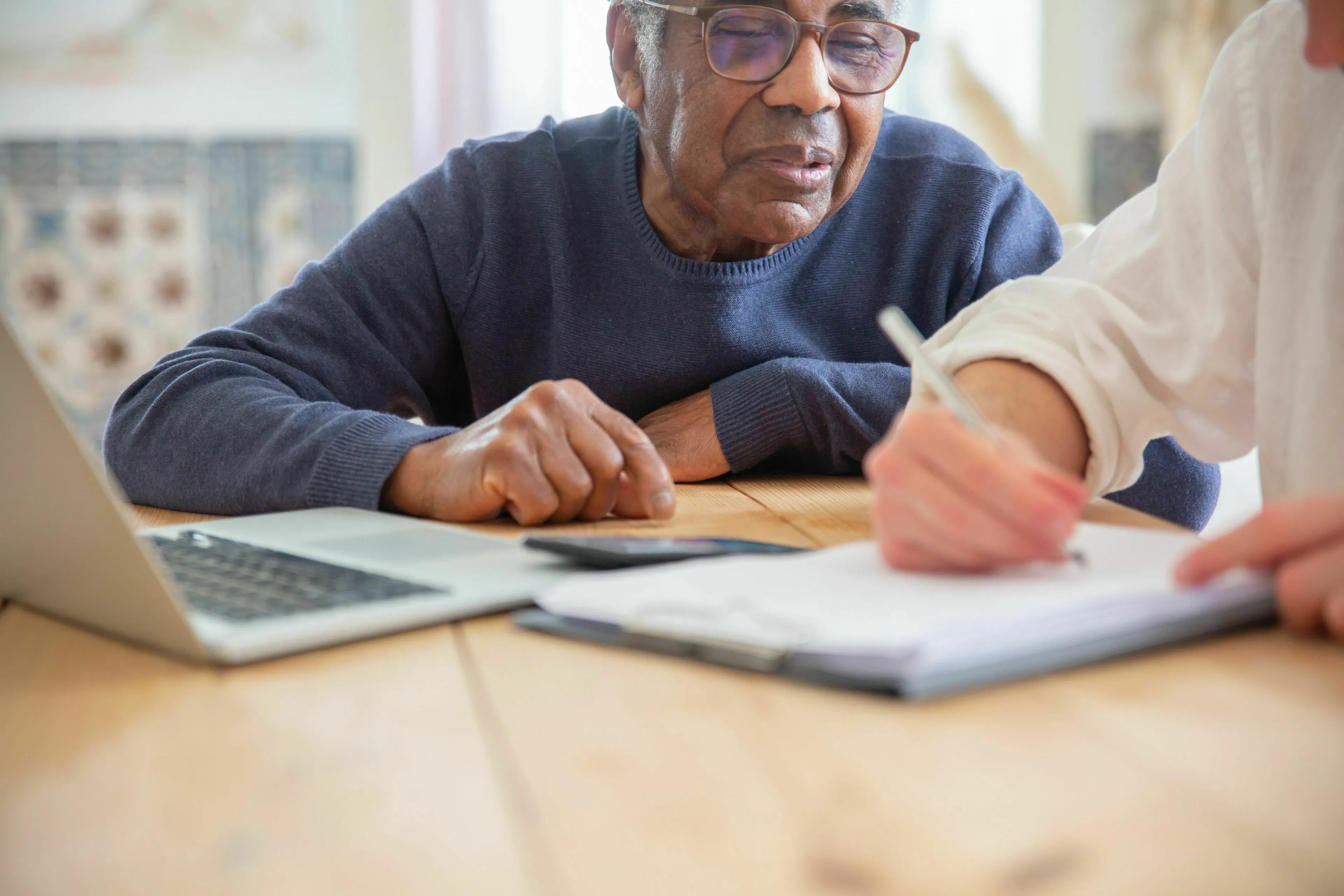 An elderly man, engaging in a general knowledge quiz, looks thoughtful while someone else writes on a document.