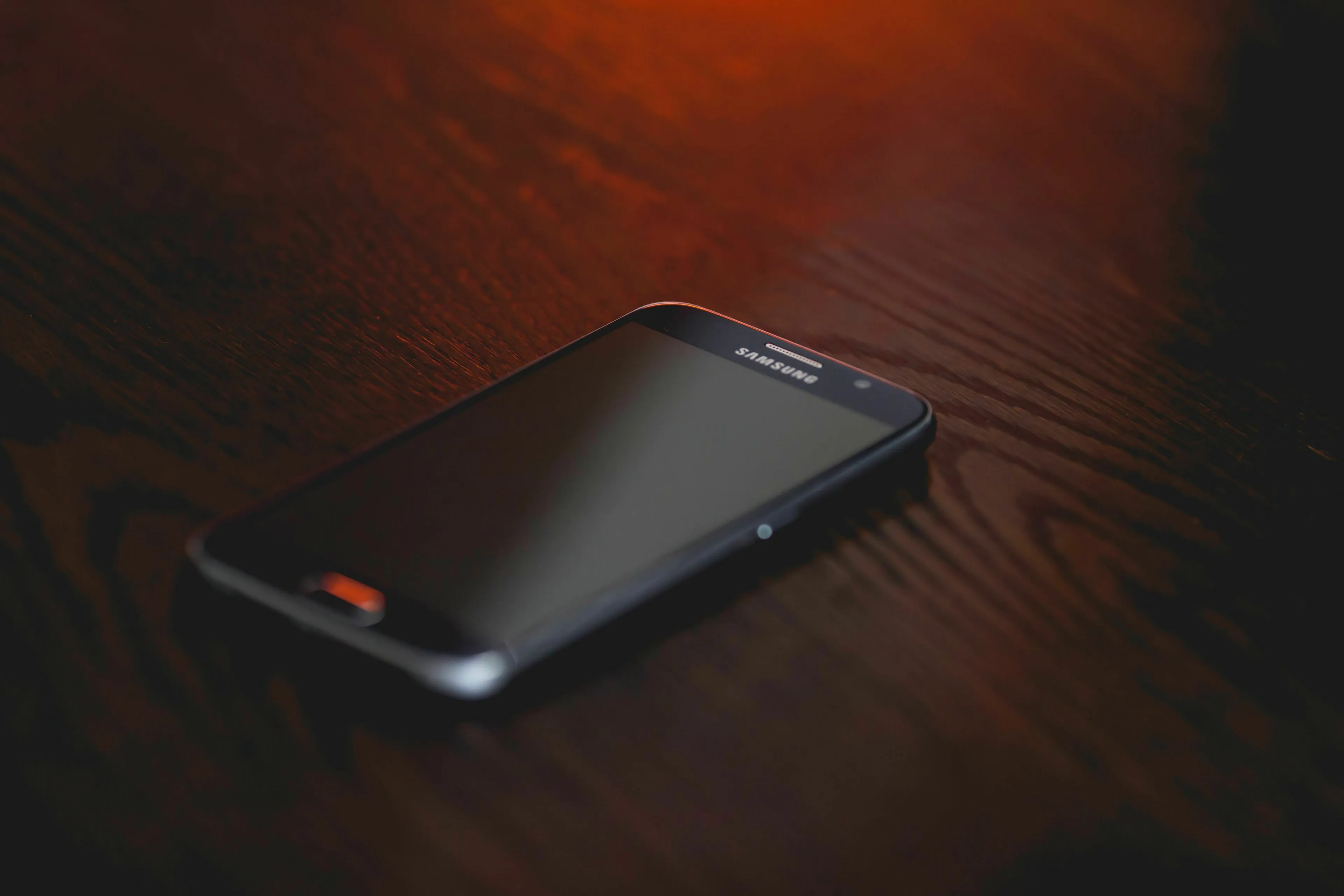 A black Samsung phone on a dark wooden table, symbolizing a silent phone and loneliness.