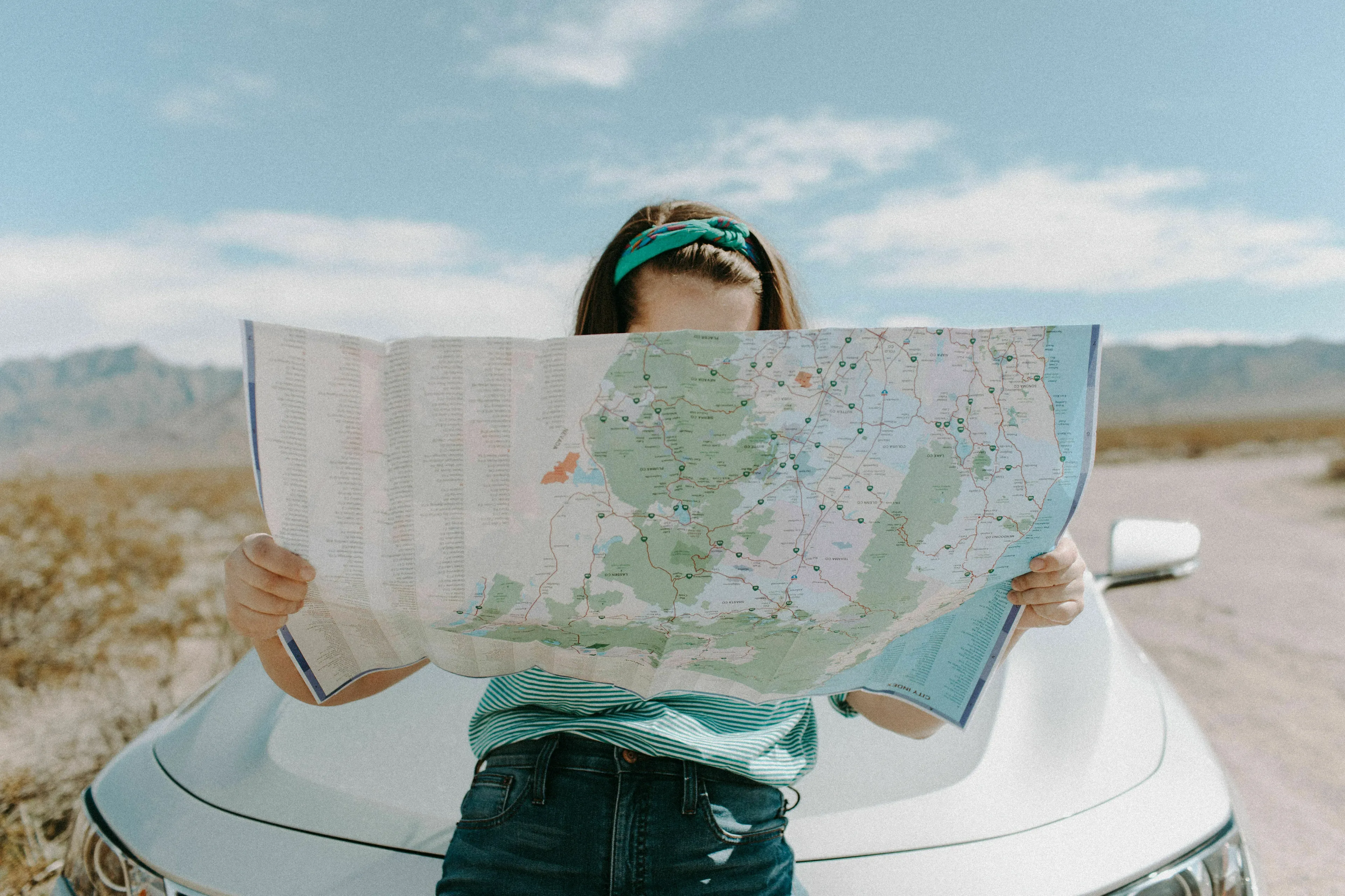 A person looking at a map in front of a car in a desert landscape during a solo road trip.