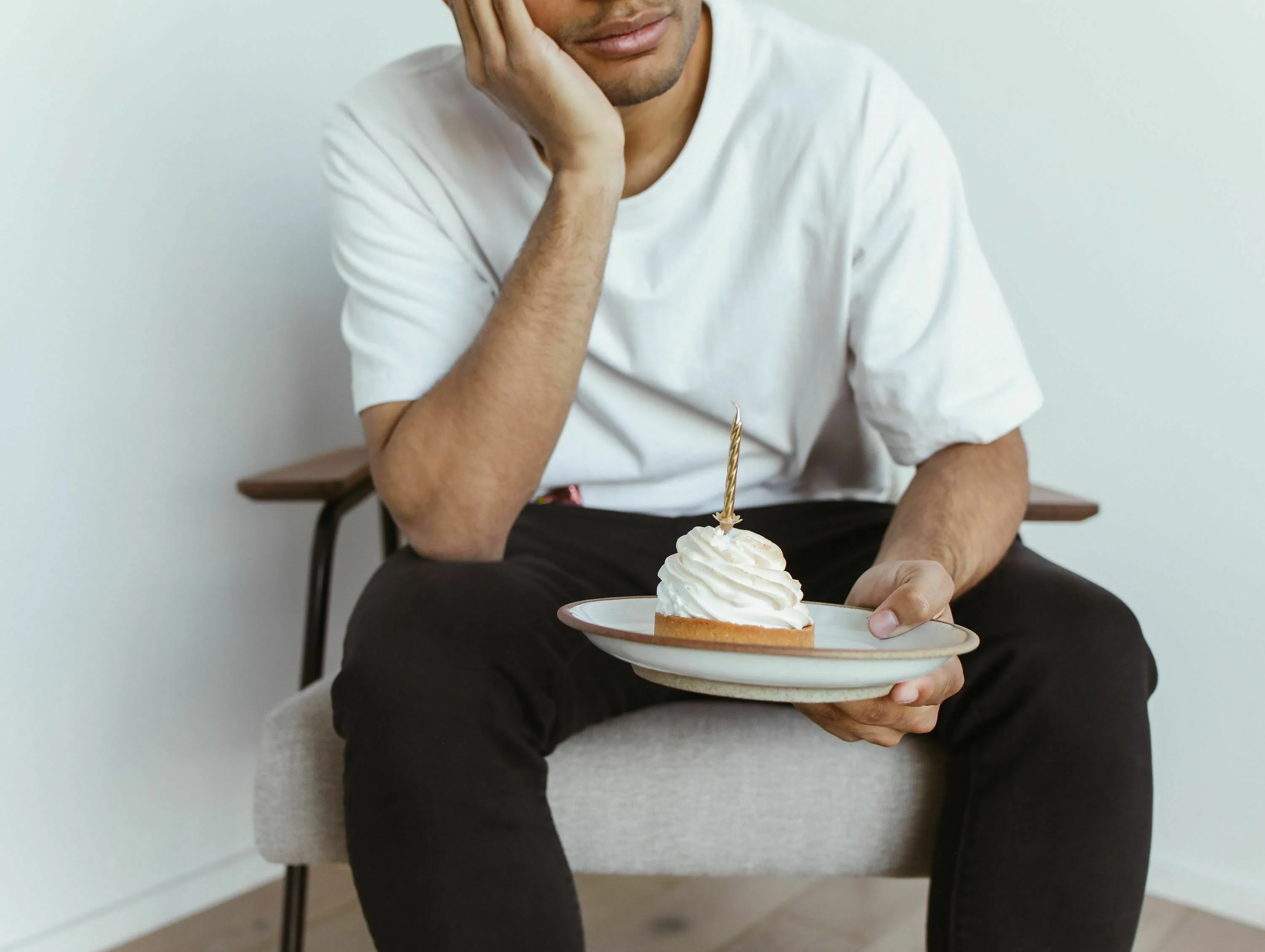 A man sitting alone with a small birthday cake, pondering how to handle loneliness on his birthday.