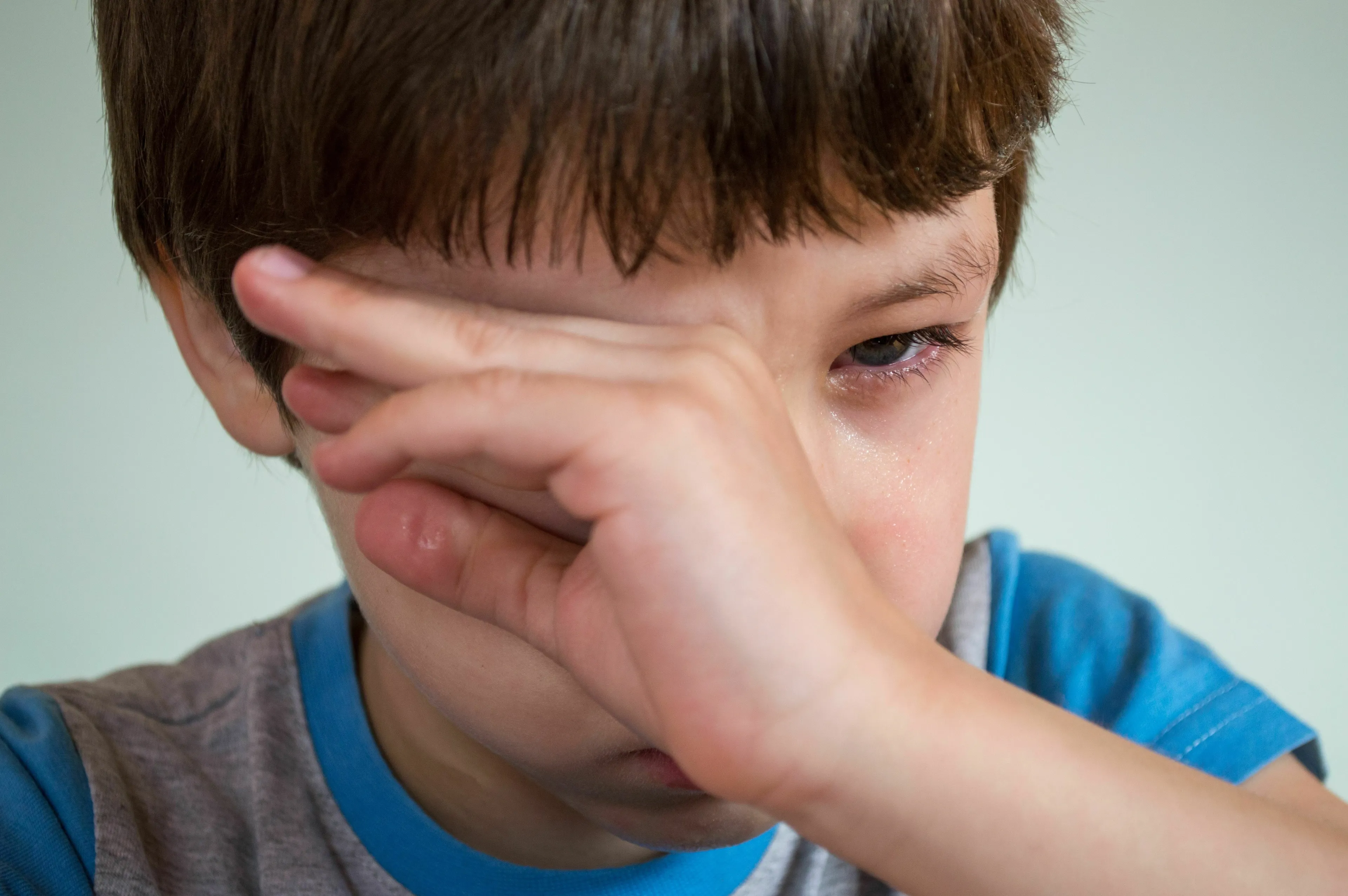 A young boy with tears in his eyes, covering his face, representing crying and how one feels after.