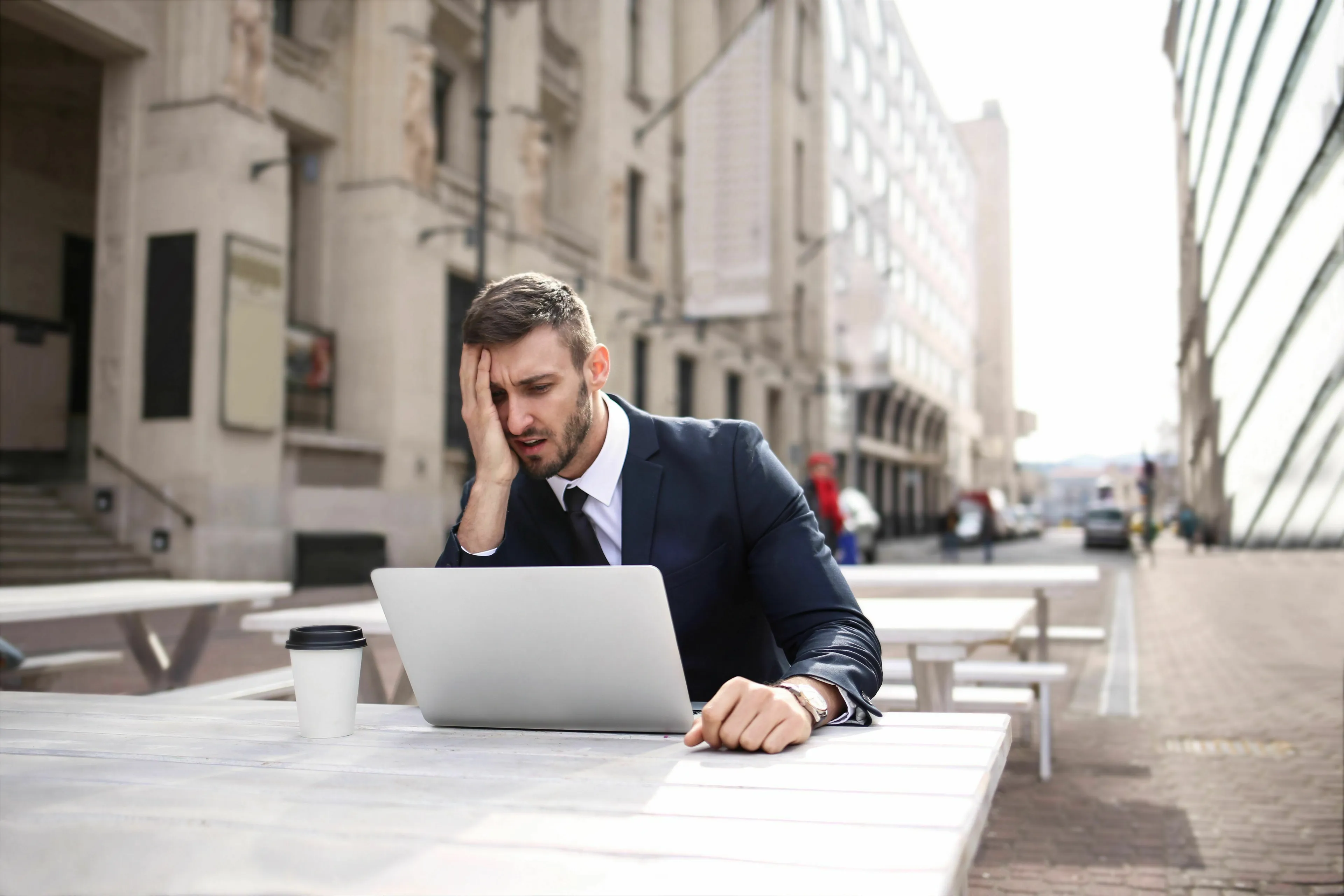 A man in a suit looking stressed at a laptop outdoors, depicting handling a bad day at work and loneliness.