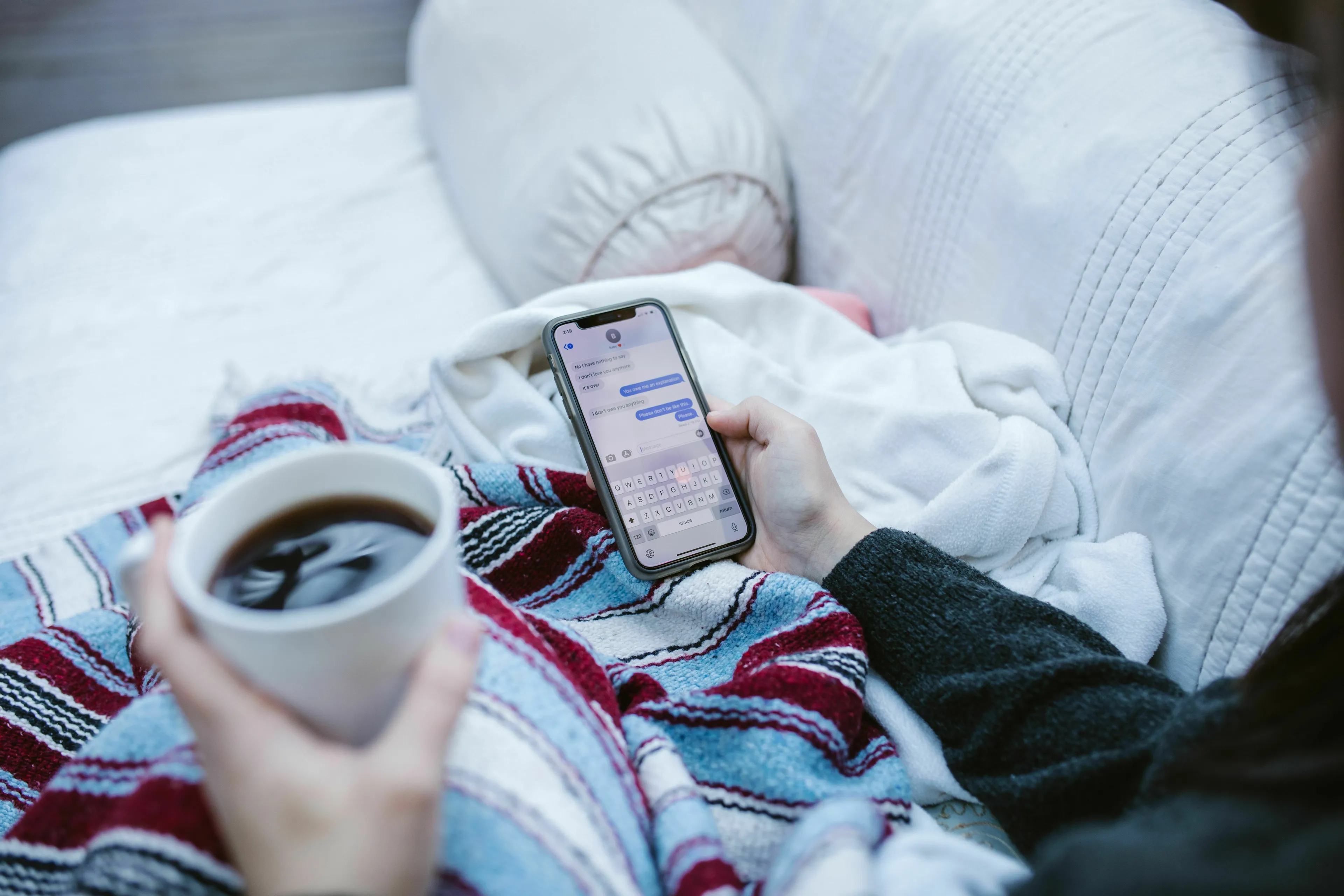A person handling loneliness, looking at a quiet friend group chat on a phone while holding a coffee.