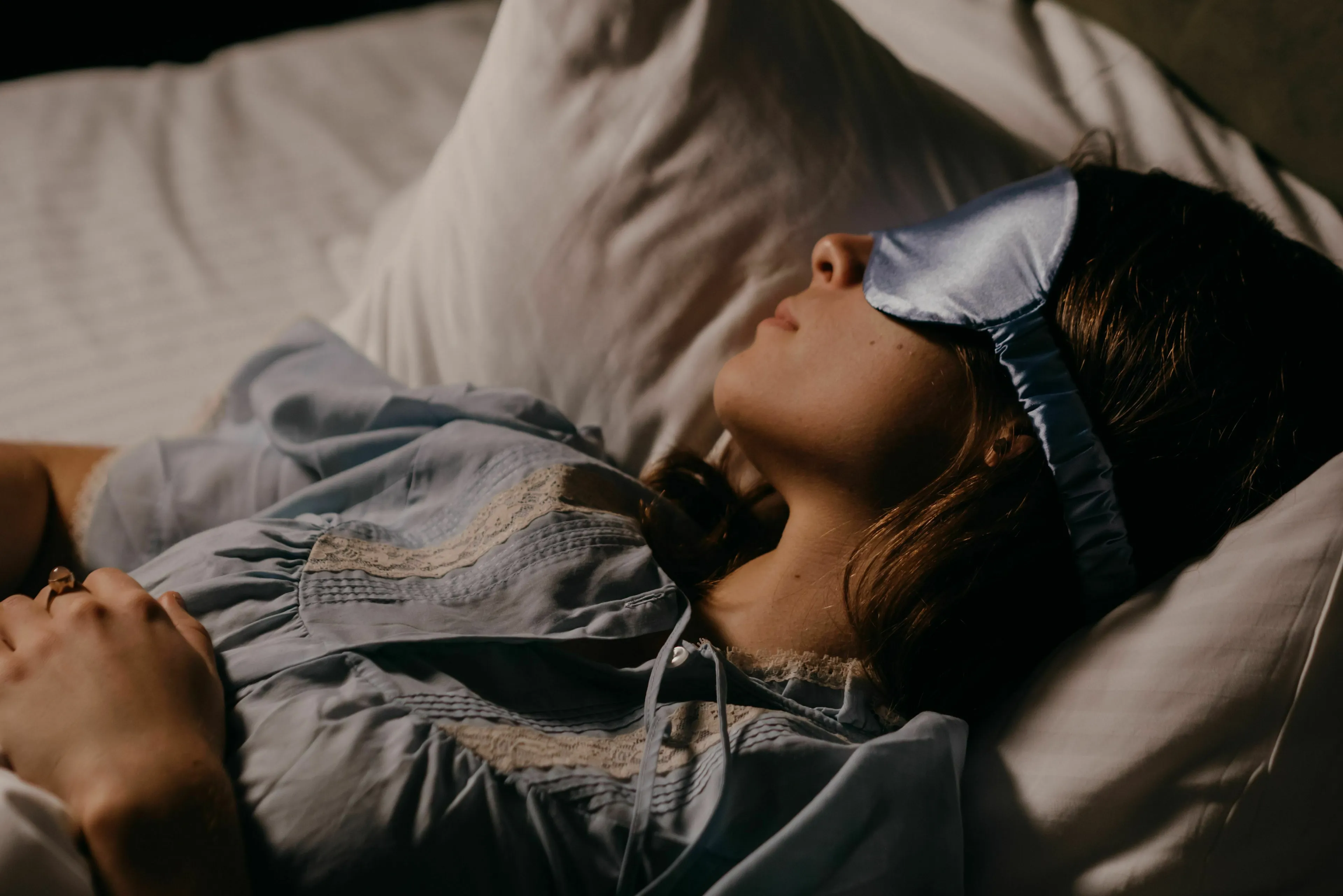 A woman wearing a sleep mask in bed, contemplating thoughts before falling asleep to handle loneliness.