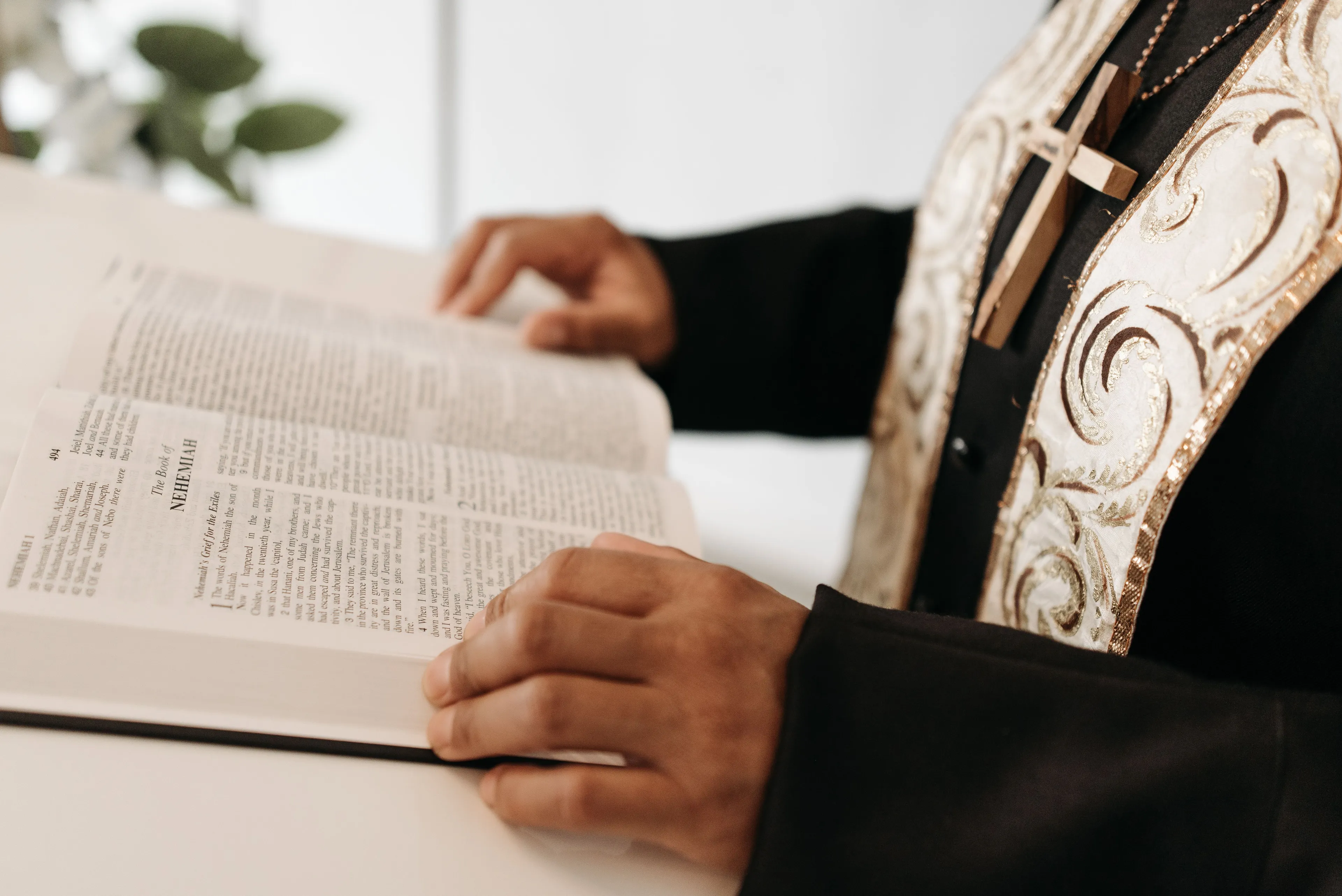 Close-up of a high priest reading from a large book, wearing a cross necklace and embroidered vestments.