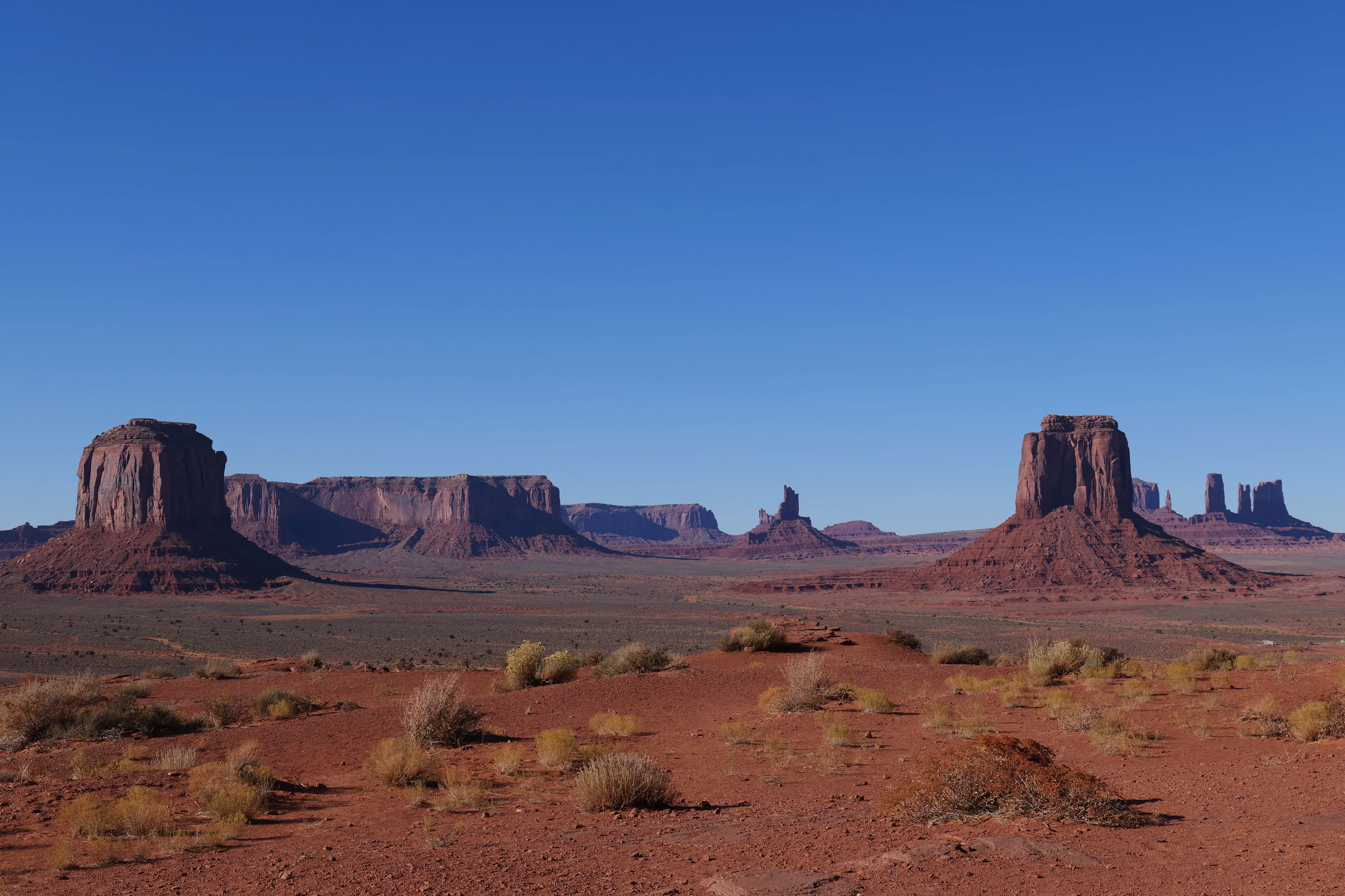 Vast highland plateau featuring Monument Valley's iconic red rock buttes and mesas under a clear blue sky.