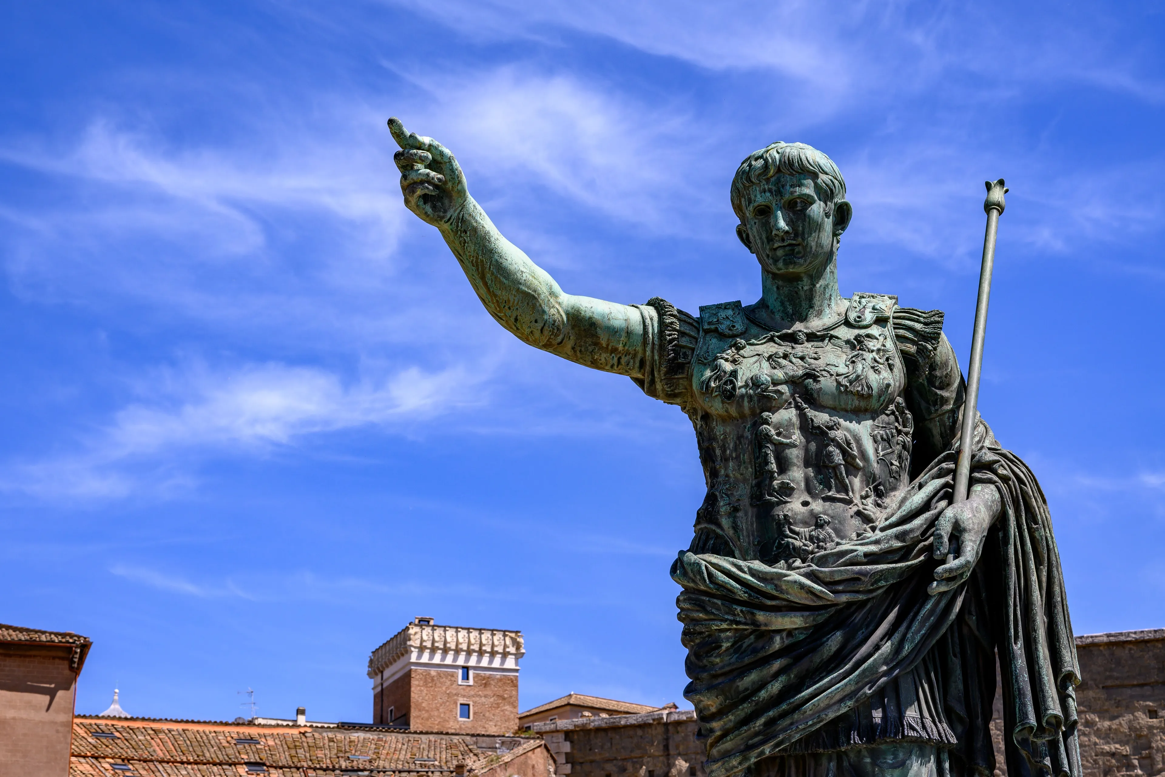 A bronze statue of Julius Caesar with arm outstretched against a blue sky, representing a historical figure to get along with.