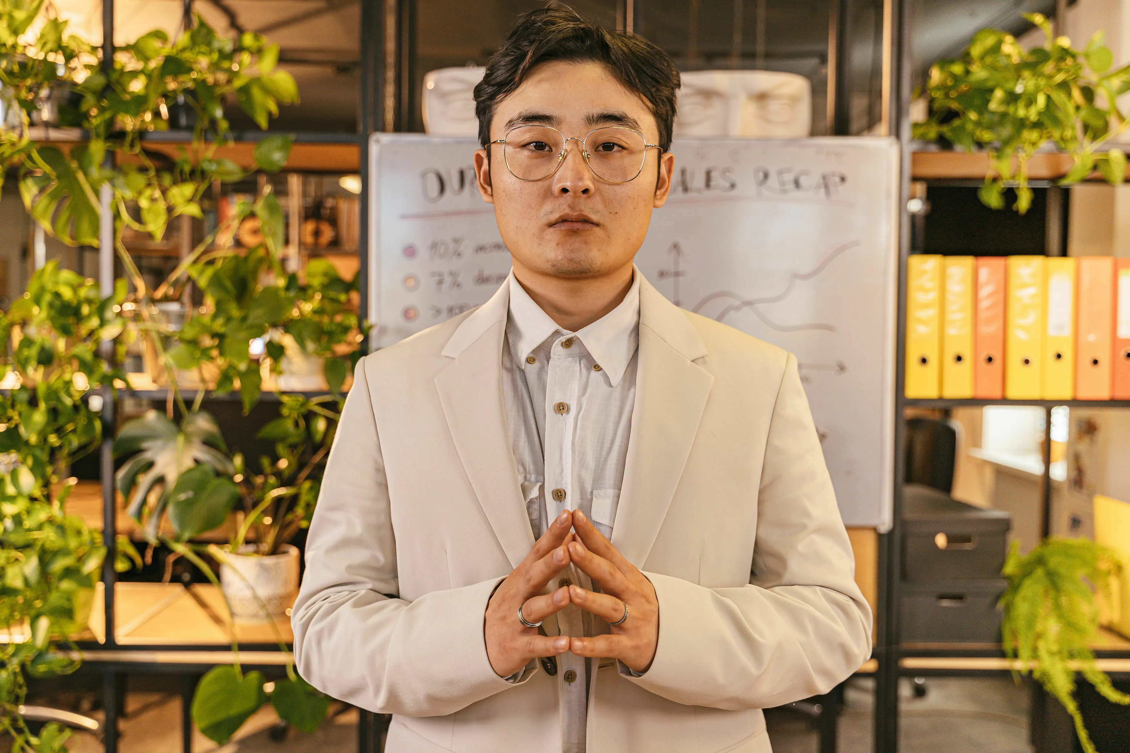Man in a suit with hands clasped, portraying a leader, in front of a whiteboard with charts.