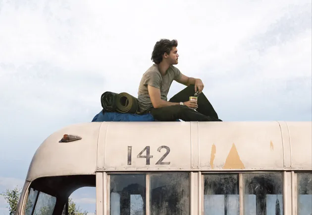 A man sitting on top of a bus, looking into the wild landscape, embodying the movie Into the Wild.