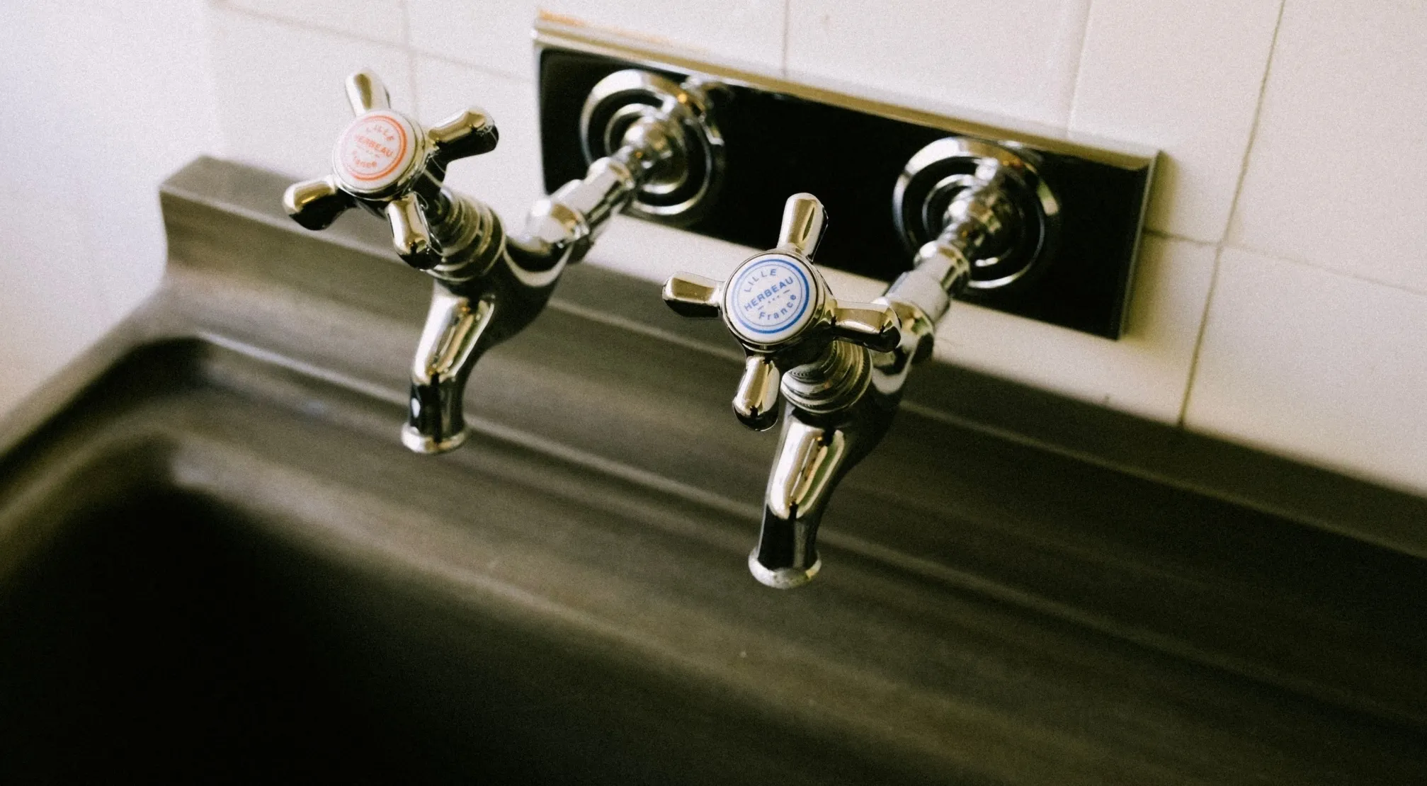 Close-up of vintage chrome American faucet handles with hot and cold labels, above a dark sink.