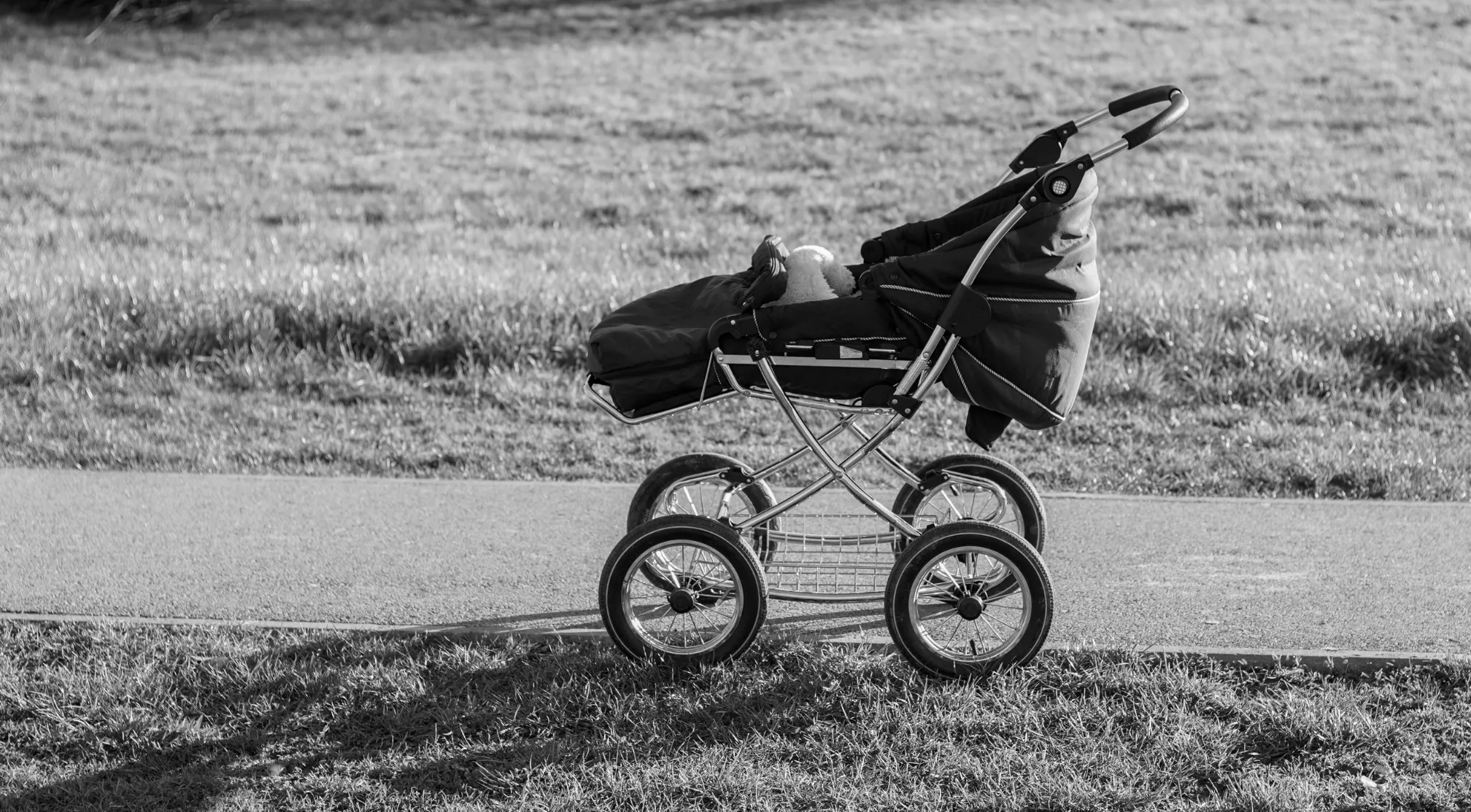 Black and white image of a pram, or British English stroller, on a path next to grass.