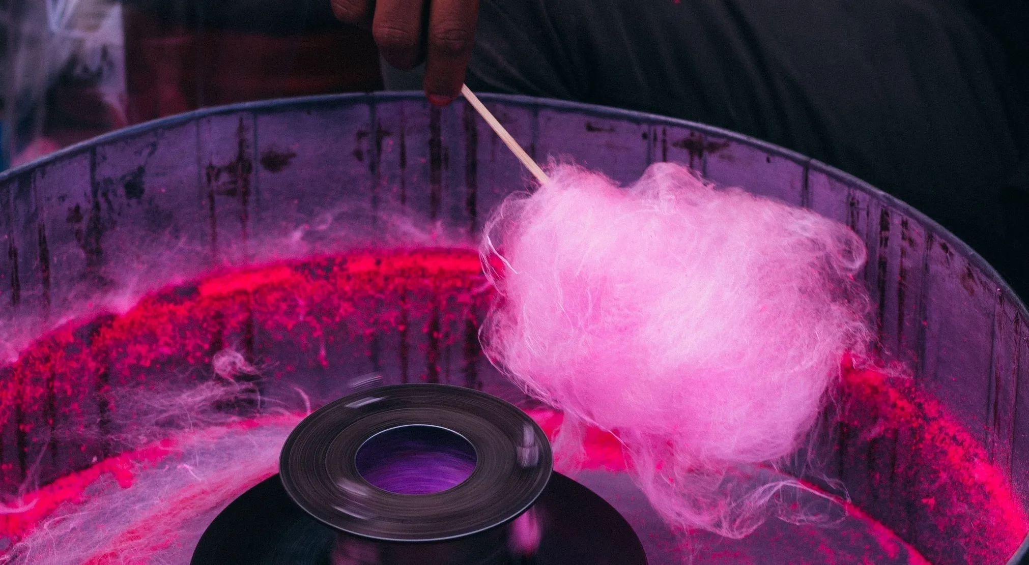 A hand collecting pink American cotton candy from a machine, with vibrant pink sugar.