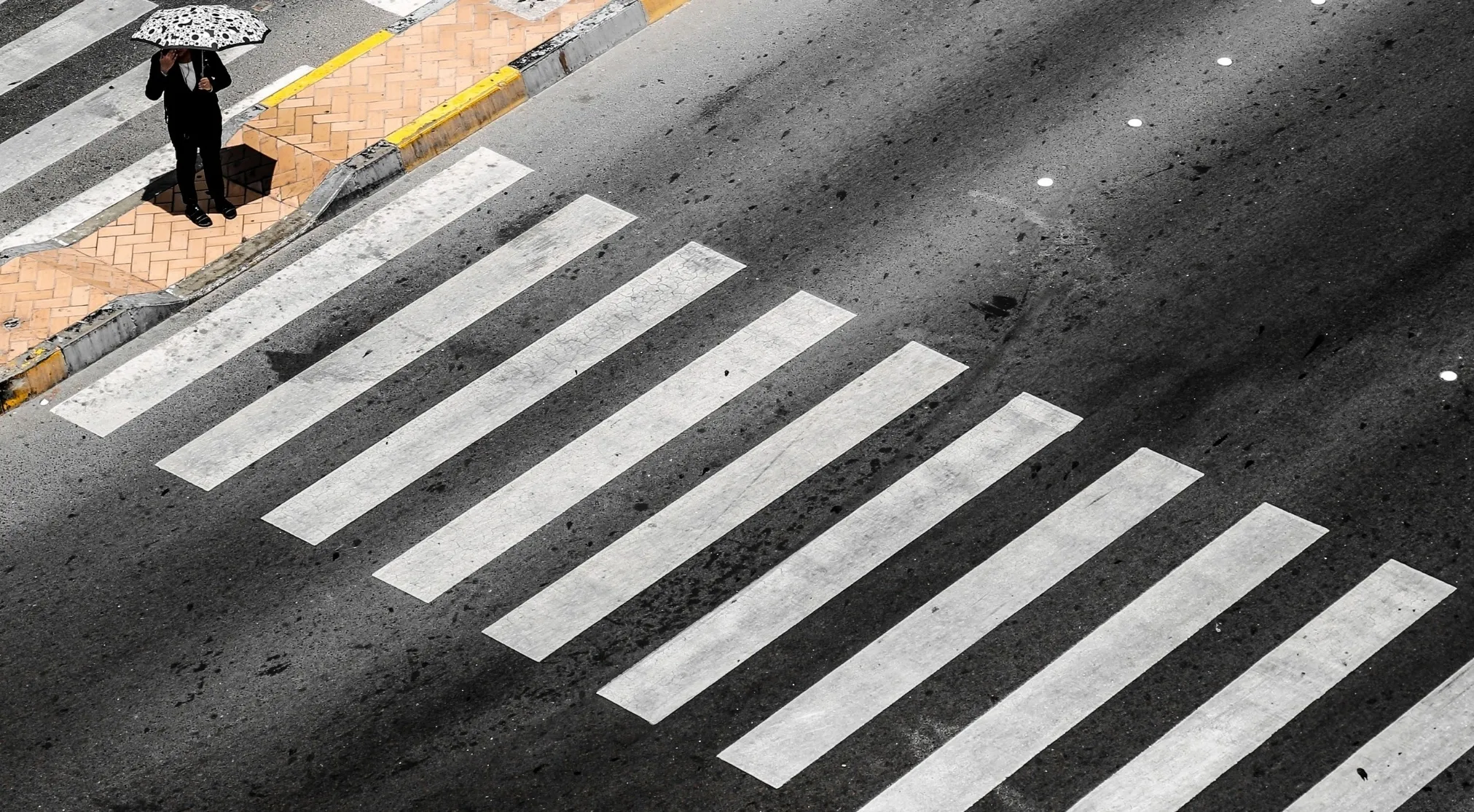 Overhead shot of a person with an umbrella on a pedestrian crossing, illustrating American vs Brit words.