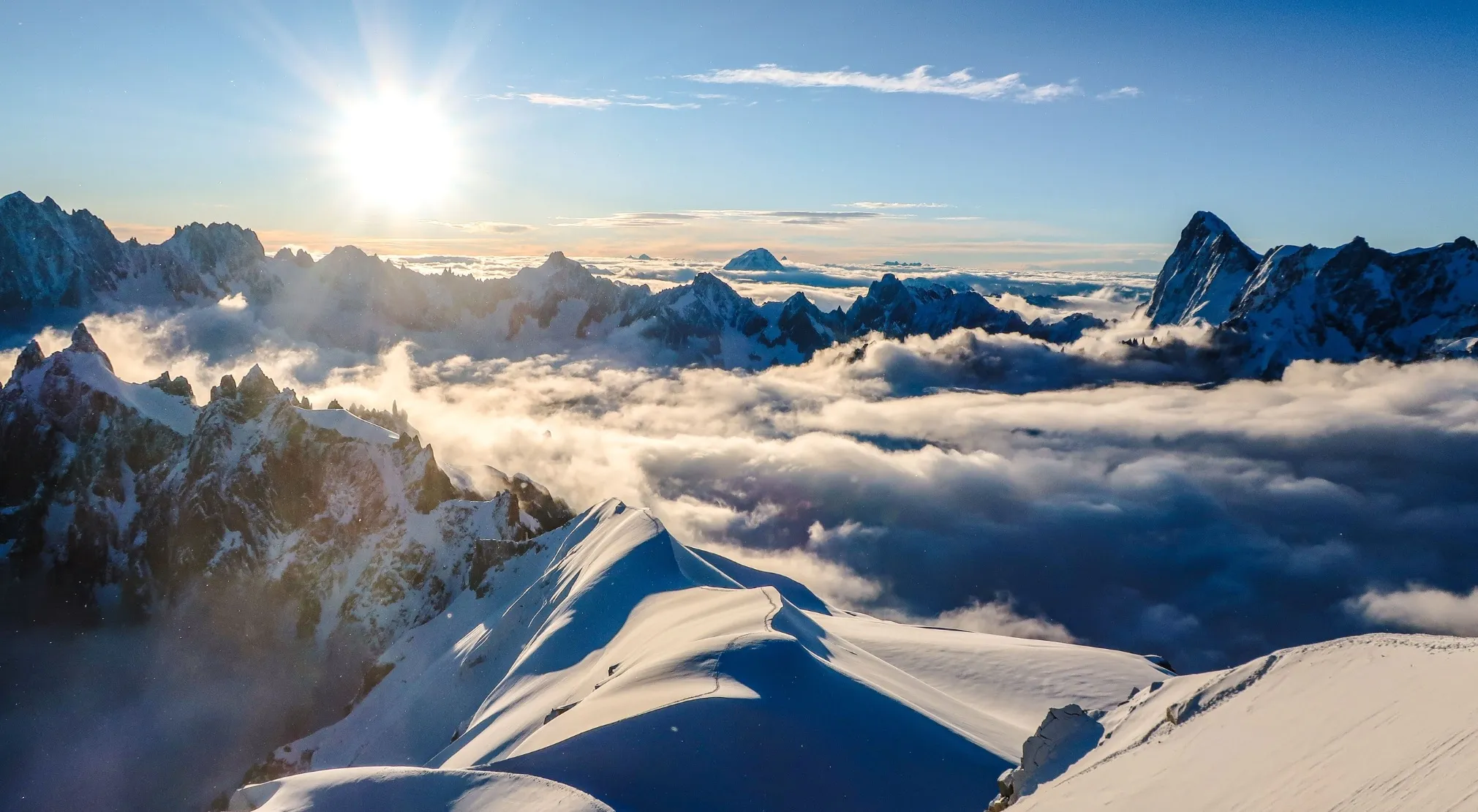 Panoramic view of snowy mountains above clouds at sunrise, showcasing the highest mountain in Western Europe.