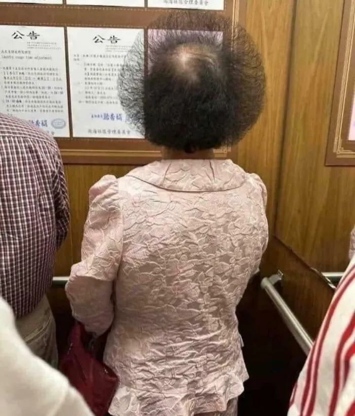 Woman with unfortunate haircuts, showcasing a highly uneven circular cut from behind in an elevator.