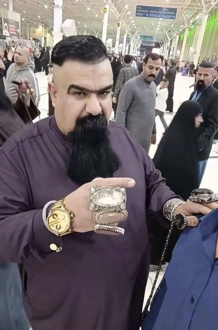 A man with a large beard, a unique shaved haircut, and many rings and bracelets on his hands.