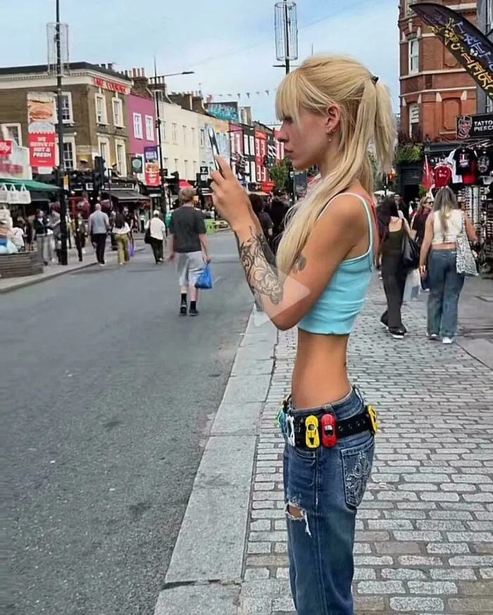 A skinny blonde woman with an edited tiny waist, showcasing Instagram Reality on a busy city street.