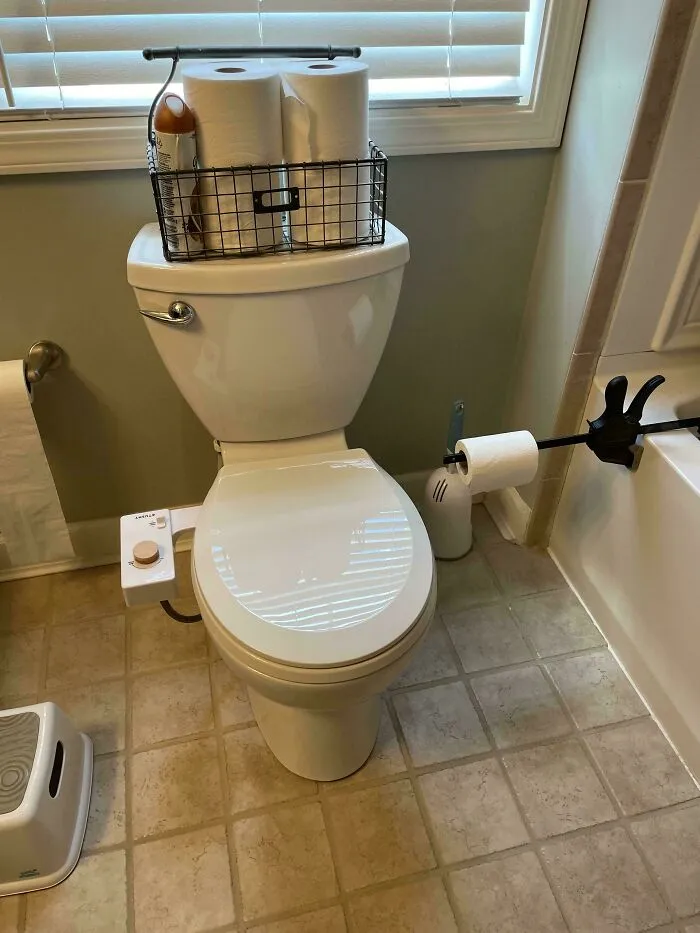 A toilet with a bidet attachment and a wire basket on top, showcasing a clever solution for bathroom organization.