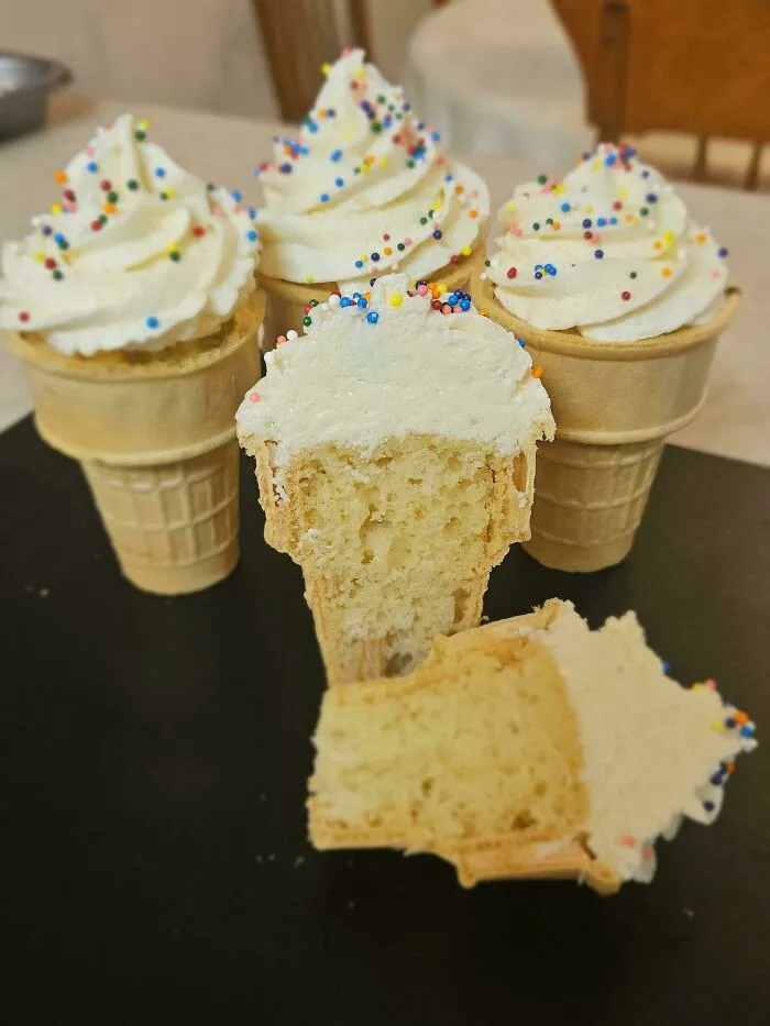Vanilla cupcakes in ice cream cones with sprinkles, one cut to show the inside, a delicious treat.