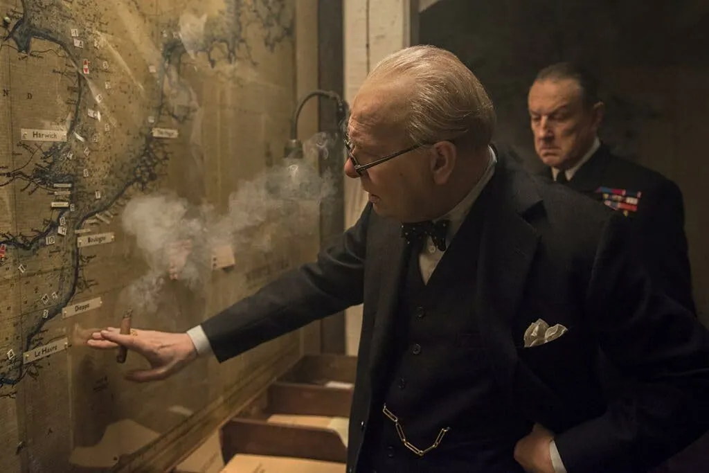 Winston Churchill smokes cigar, looking at a map. Darkest Hour (2017) historical event.
