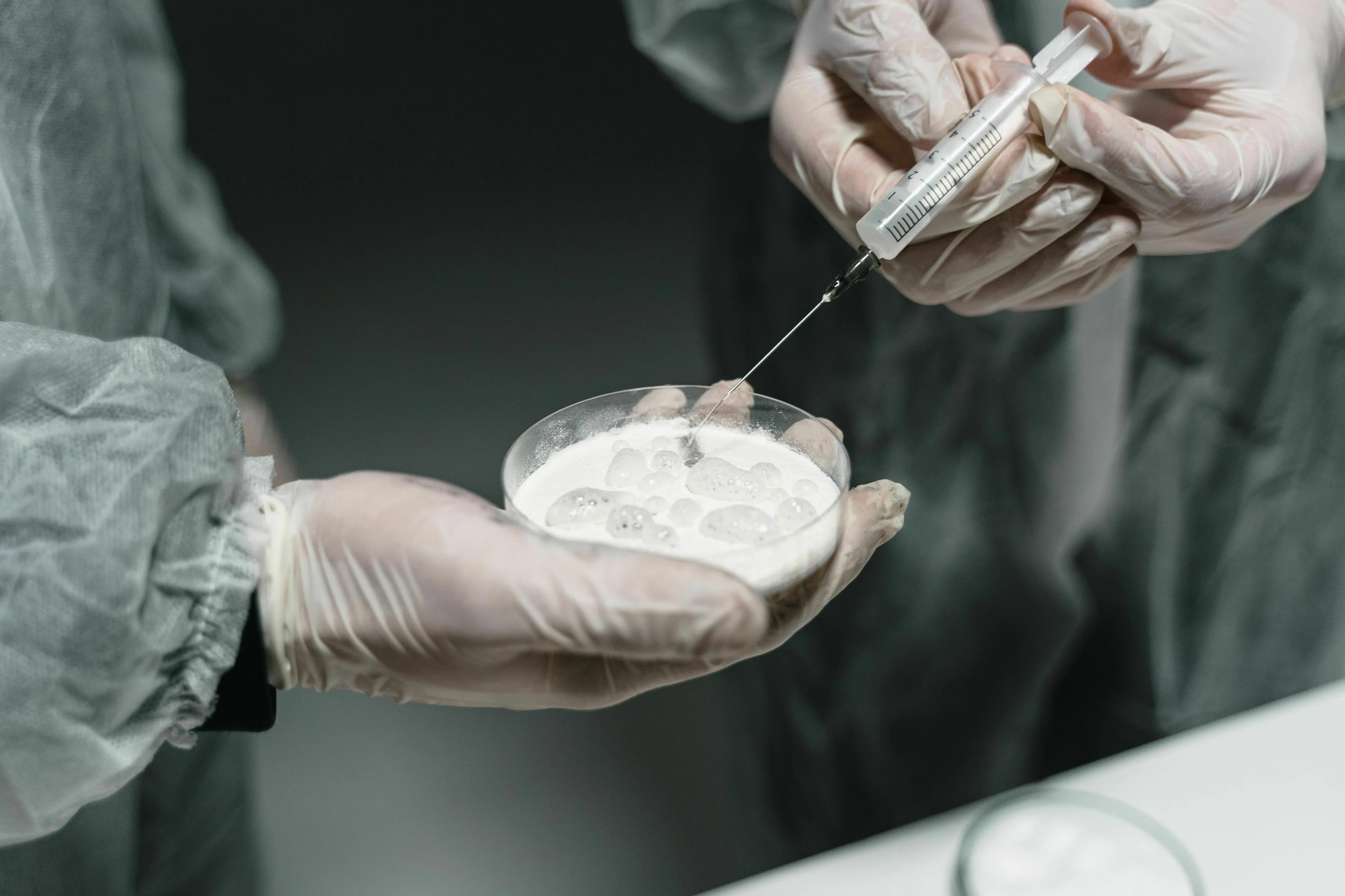 Basic Medical Knowledge Quiz: A person in a lab coat and gloves extracting fluid with a syringe from a petri dish.