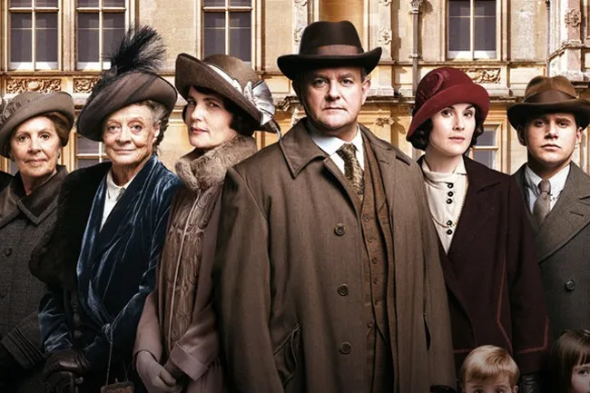 The distinguished cast of Downton Abbey standing in front of the grand estate.